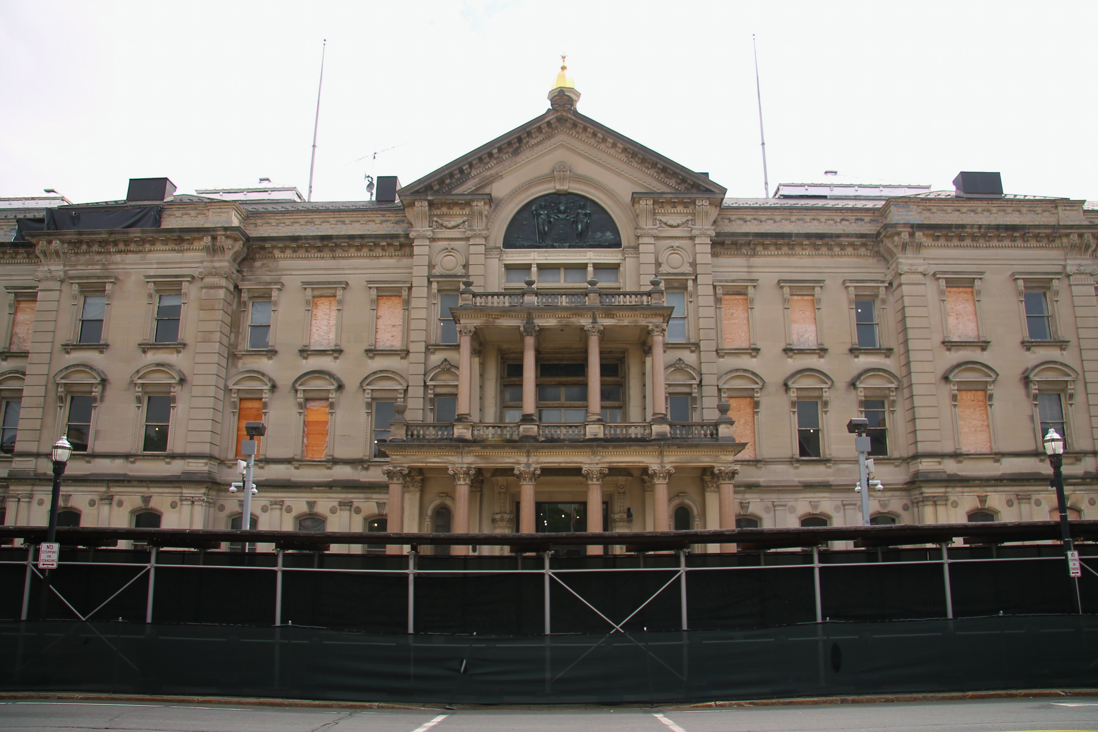 Neoclassical state capitol building with gold dome and columns, surrounded by construction fencing.