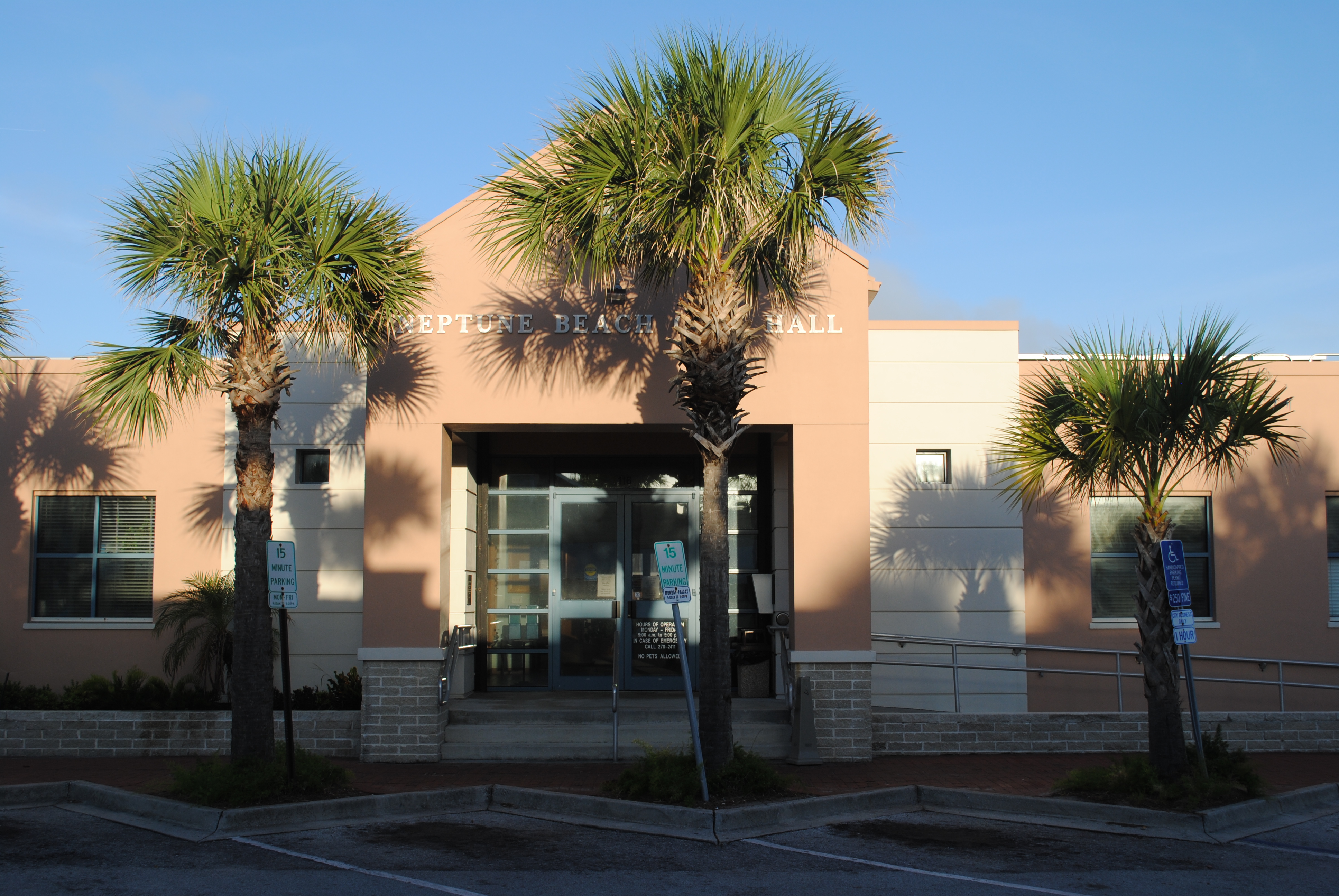 Single-story tan stucco building with palm trees and a city hall sign at the entrance.