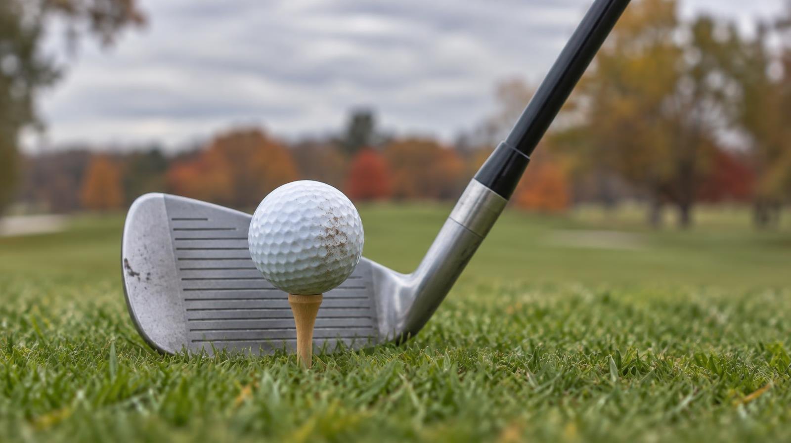 A golf ball on a tee with an iron club head positioned behind it on a green fairway.