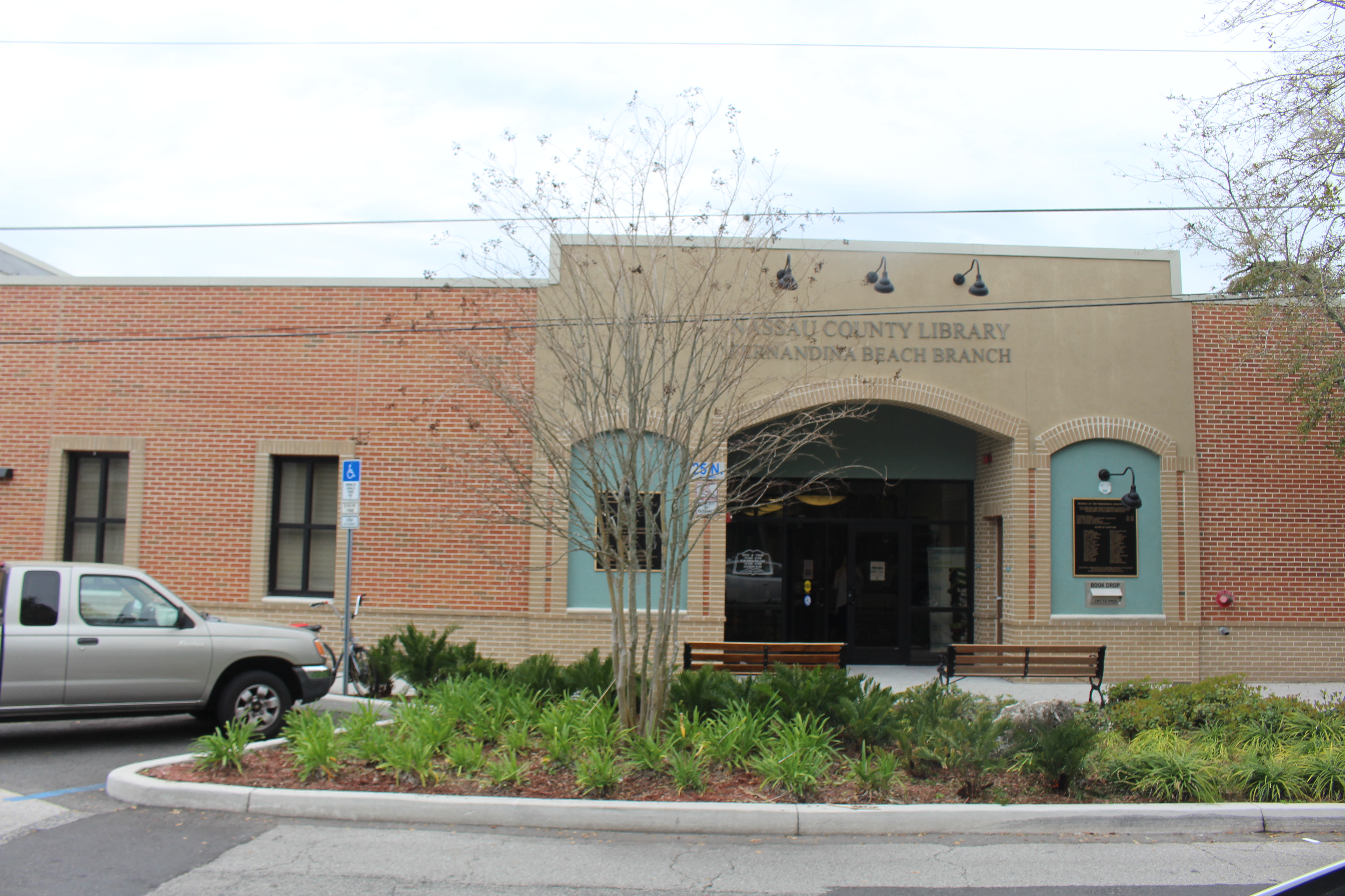 Exterior of a single-story brick public library building with a covered entrance and landscaping.