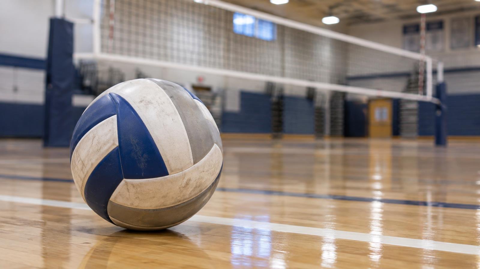 A volleyball resting on a hardwood gym floor near a net.