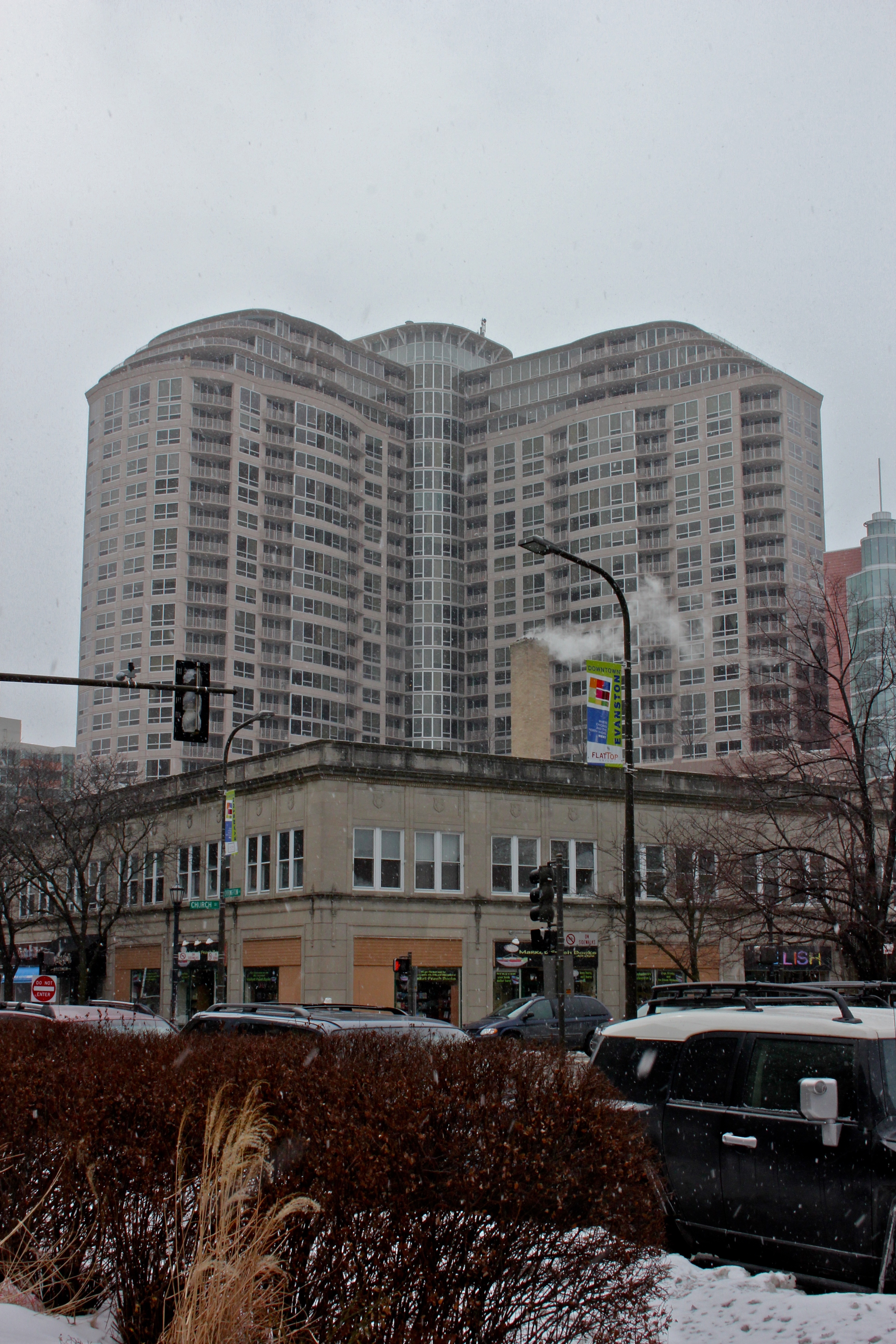 A high-rise apartment building with a curved facade on a snowy overcast day in an urban setting.