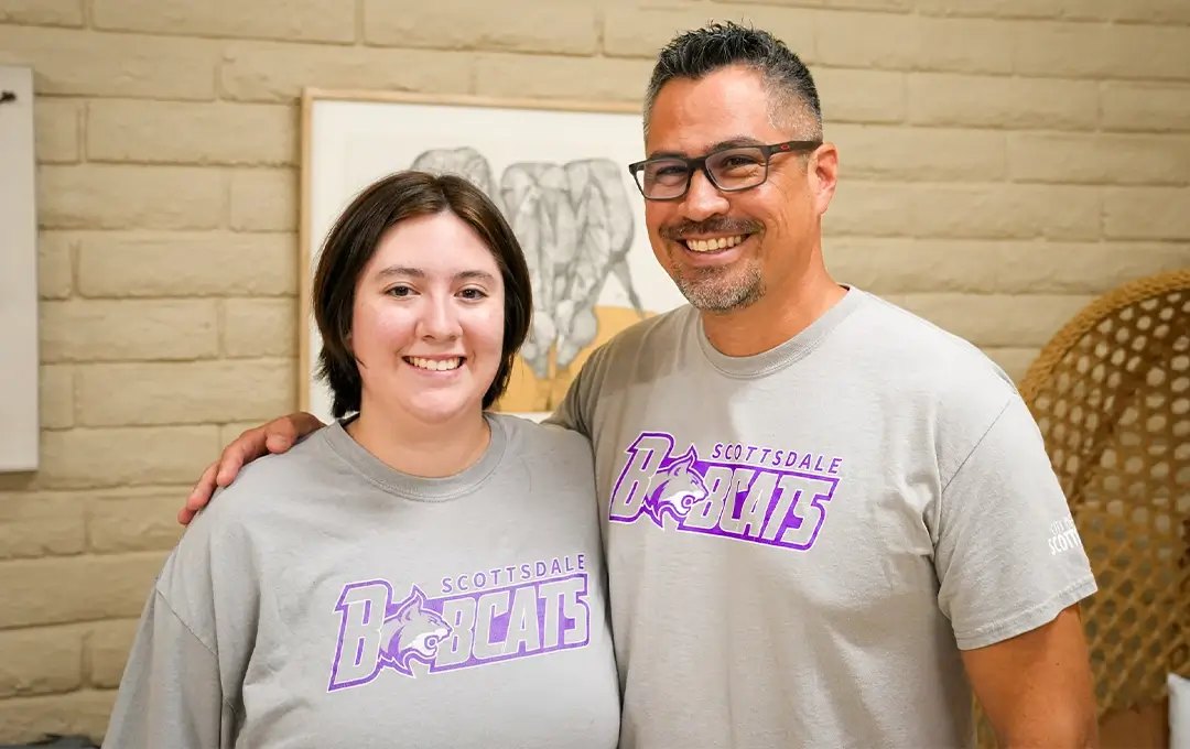 Two smiling adults wearing matching gray Scottsdale Bobcats t-shirts pose indoors.