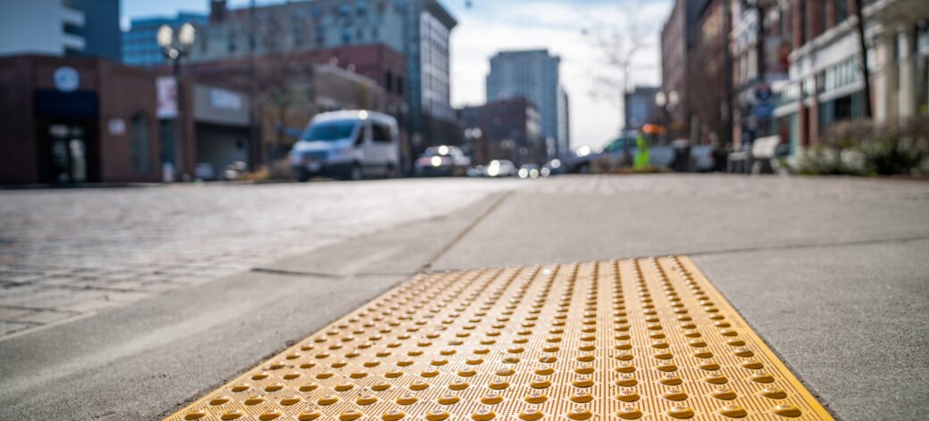Yellow raised-dome tactile warning strip embedded in a concrete sidewalk curb cut.
