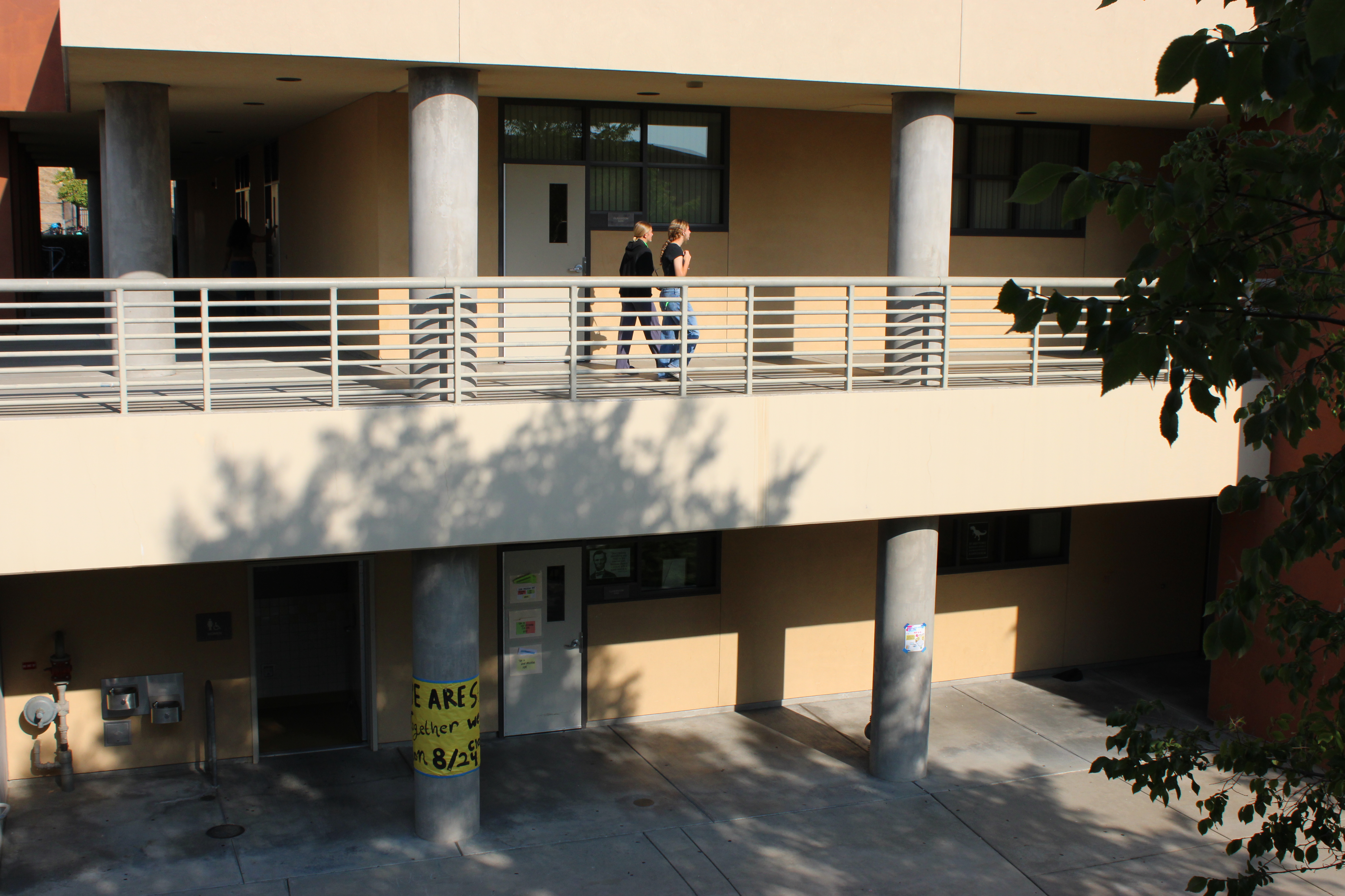 Two students walking along an outdoor second-floor corridor of a school building.