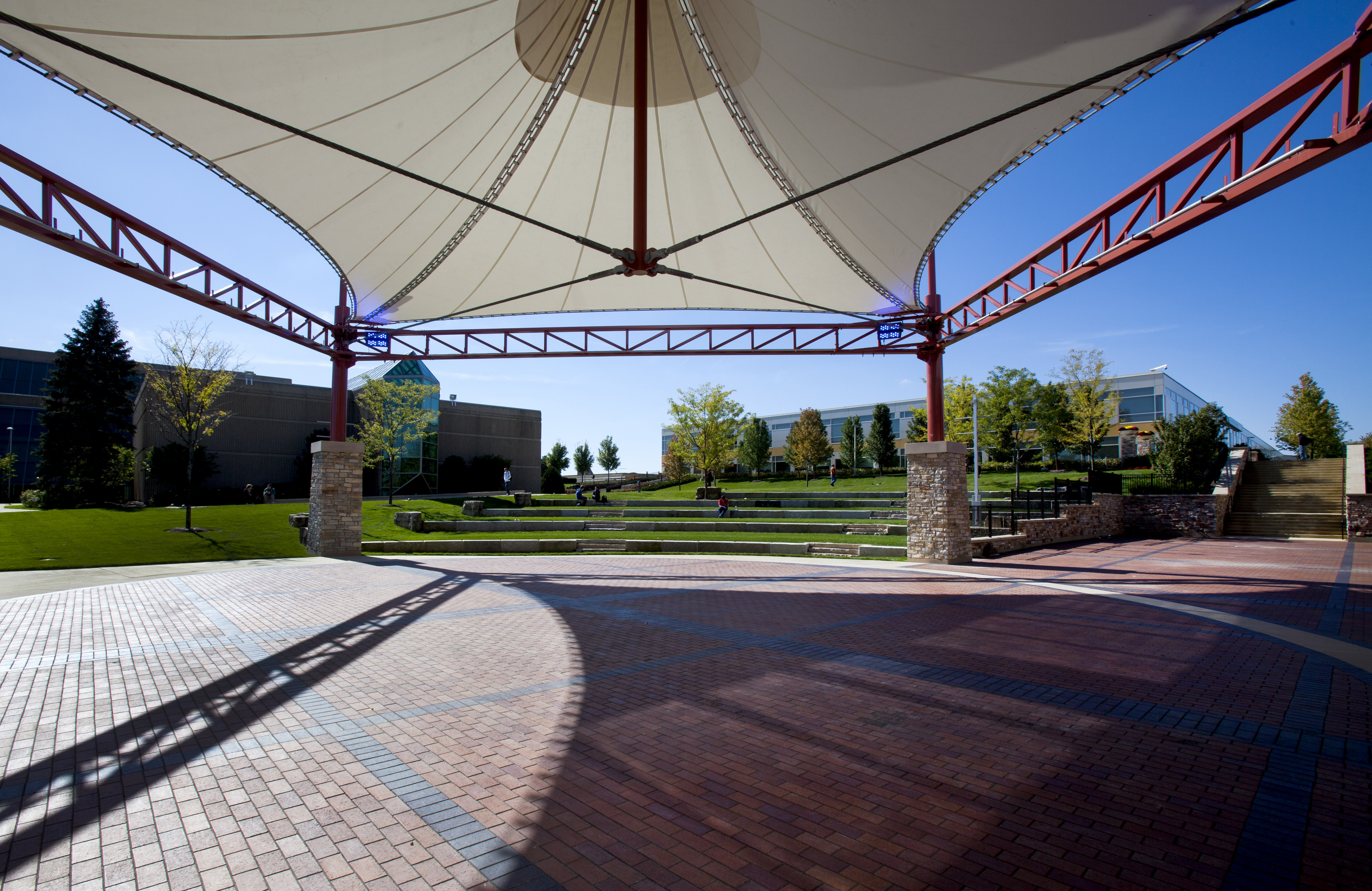 Outdoor courtyard with a white fabric canopy and red steel trusses at a college arts center.