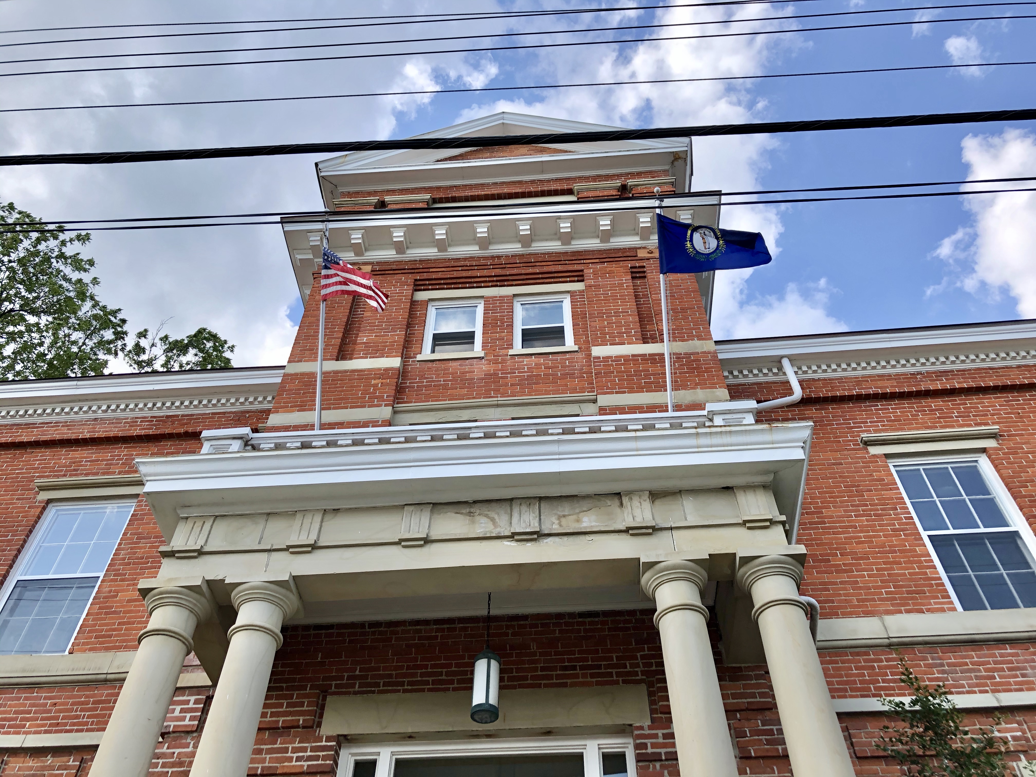 Low-angle view of a red brick courthouse with white columns and two flags against a blue sky.