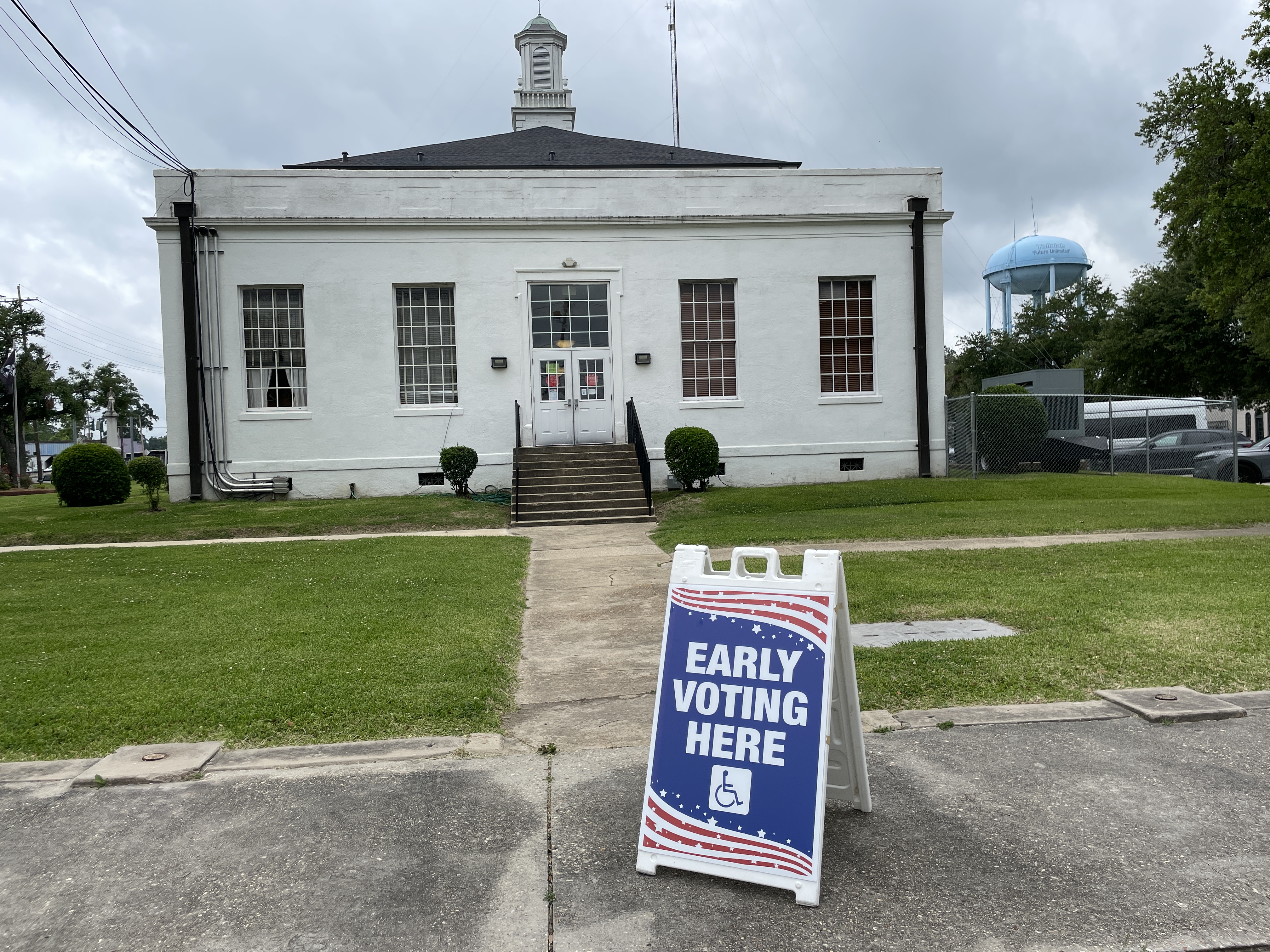Blue sandwich board sign reading 'Early Voting Here' in front of a white government building with a cupola.
