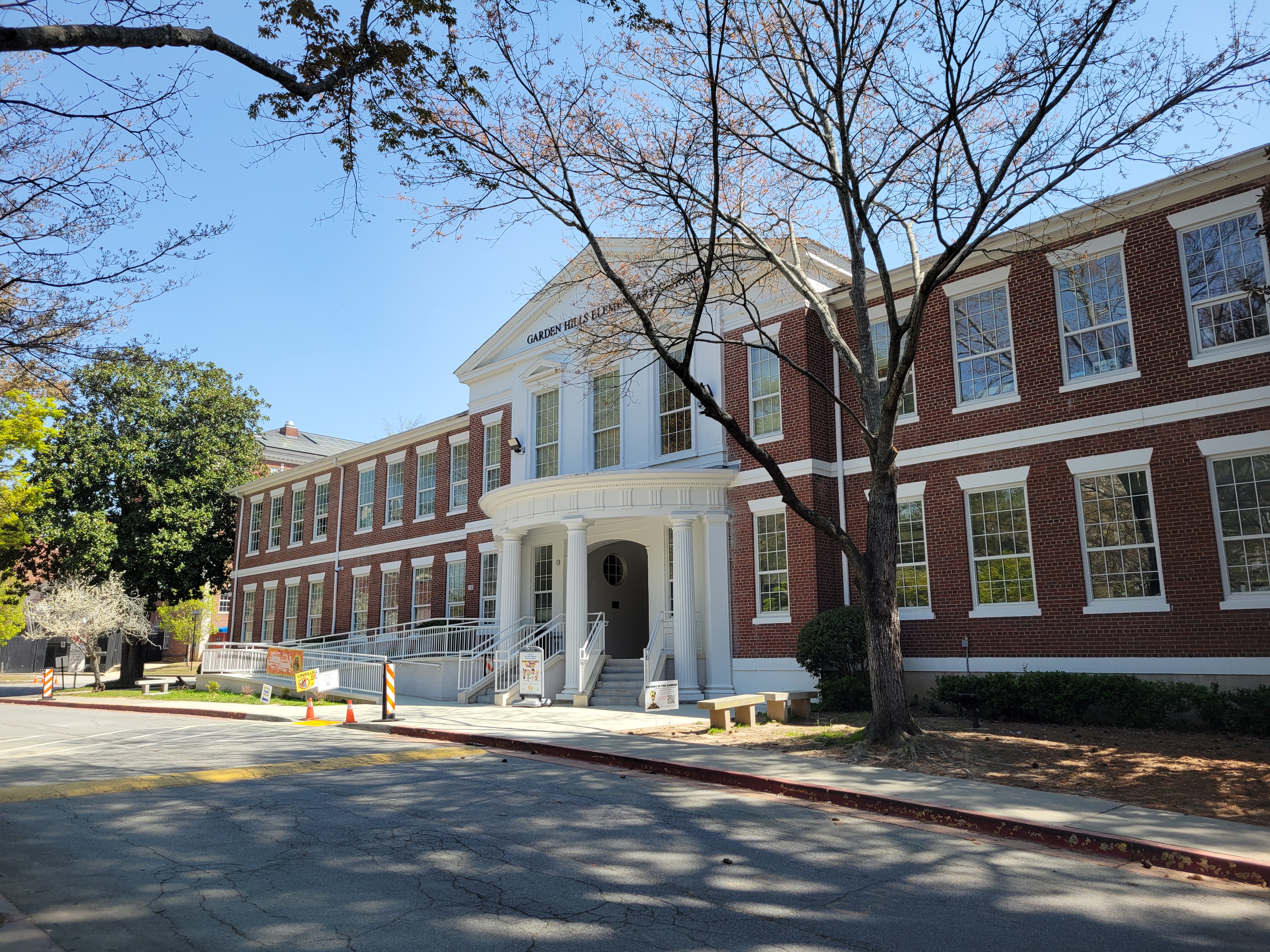 Two-story red brick elementary school building with white columned entrance and trees in front.