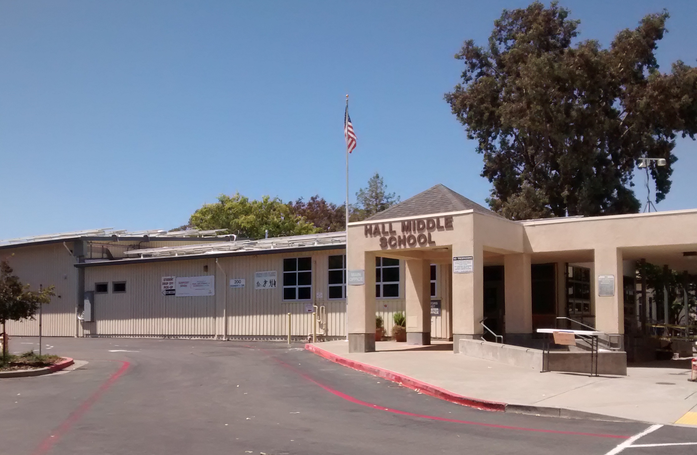 Single-story school building exterior with flagpole and parking lot under a clear blue sky.
