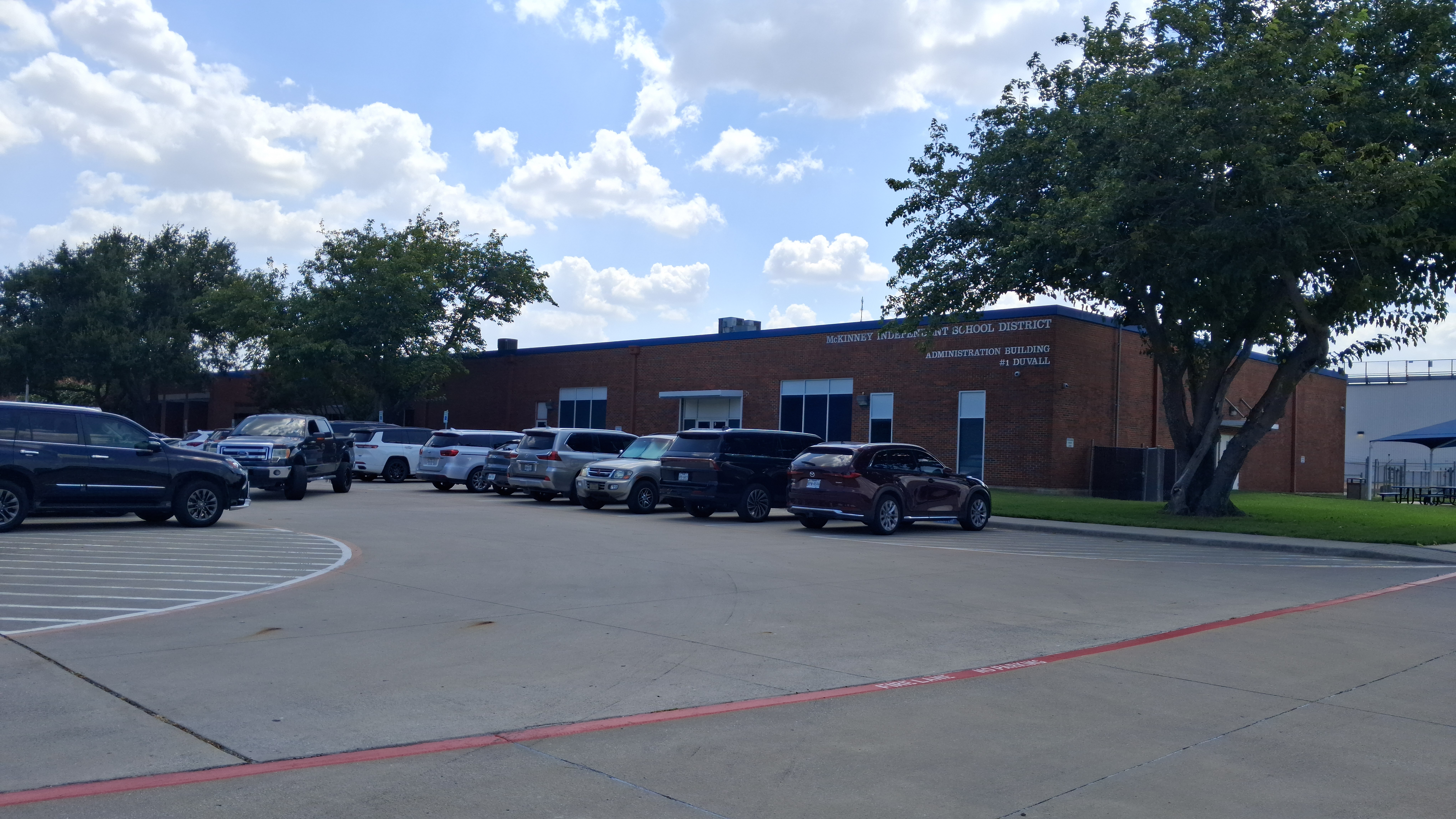 Large school district administration building with a parking lot in front.
