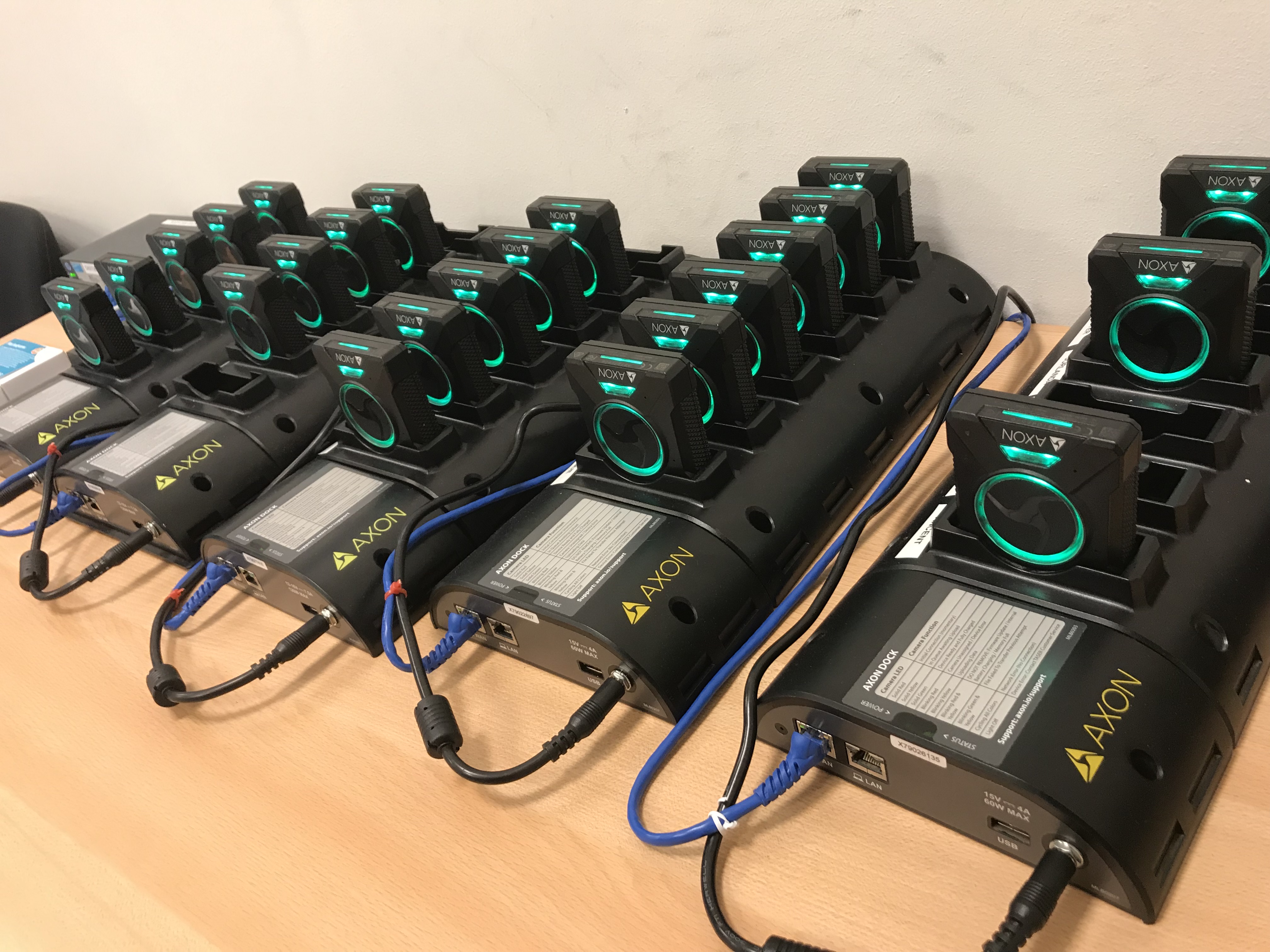 Multiple Axon body cameras in black charging docks on a desk.