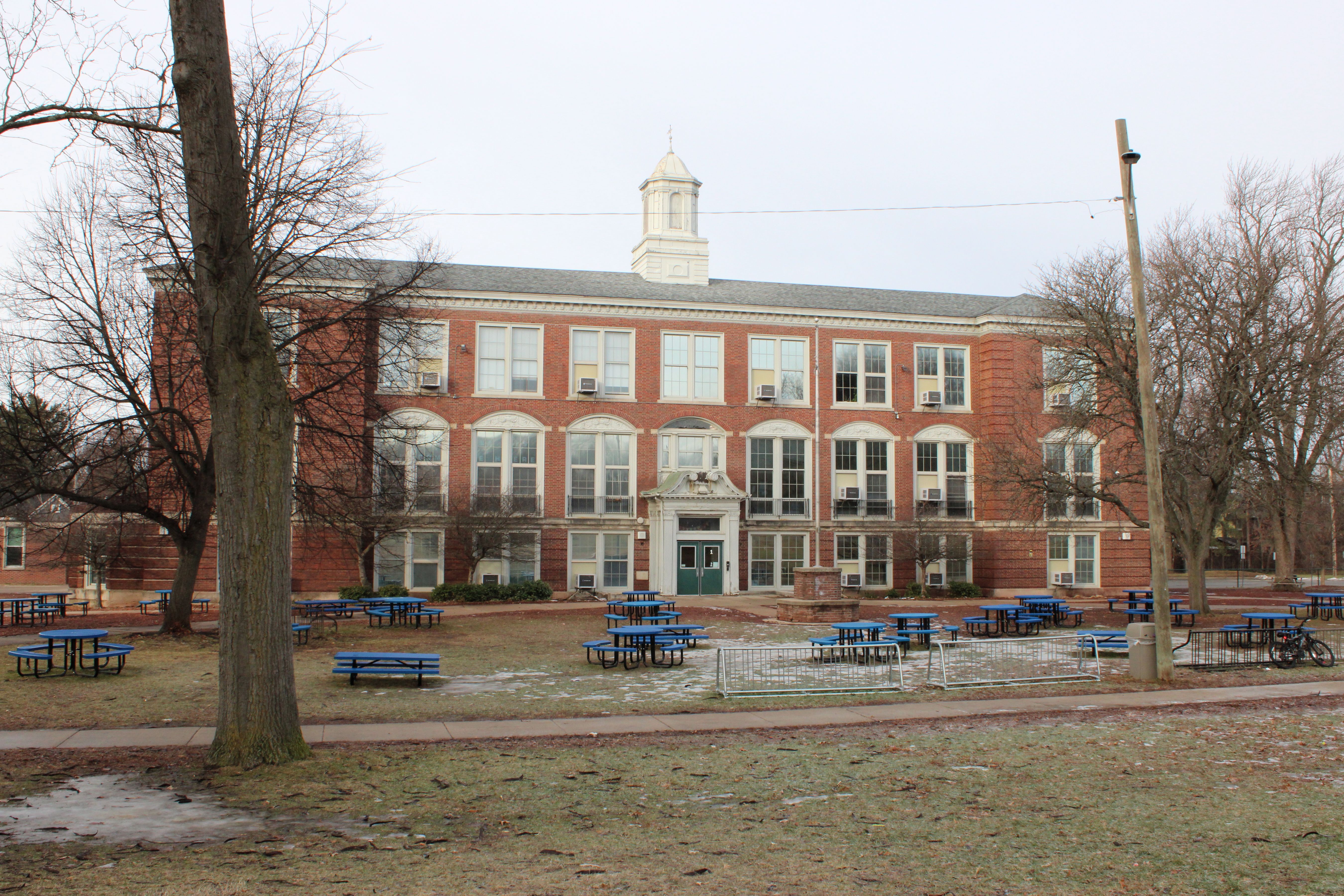 Three-story red brick school building with white cupola and bare winter trees.