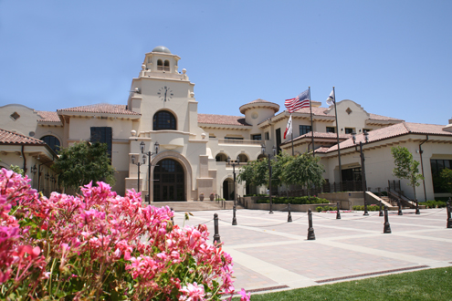 City hall exterior with clock tower, red tile roof, and American and California state flags.