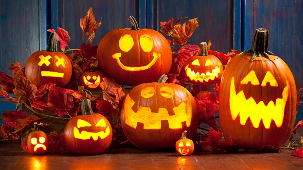 Several glowing carved jack-o'-lanterns surrounded by autumn leaves on a wooden surface.