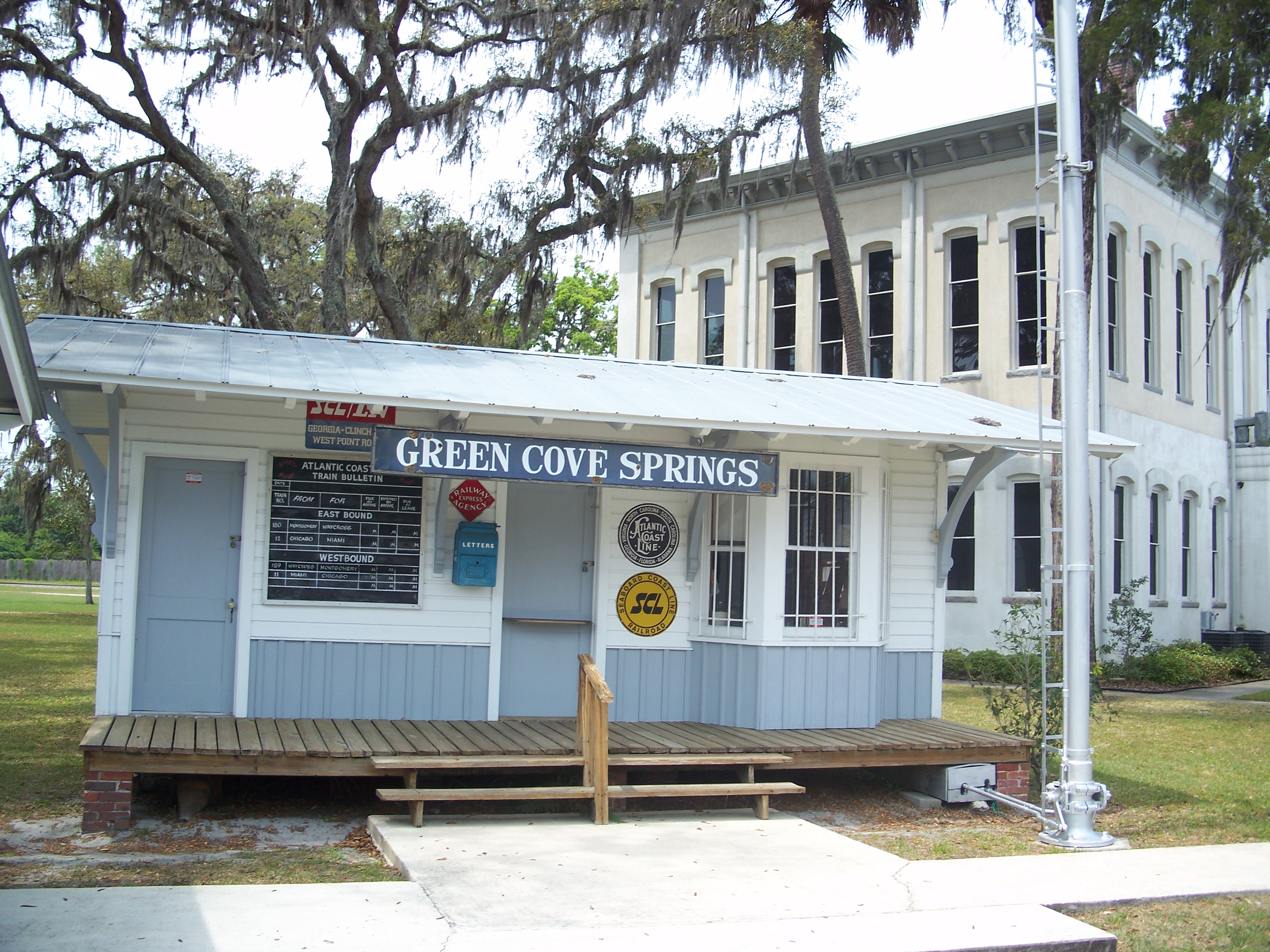 Historic depot building and two-story courthouse amid Spanish moss-draped trees.