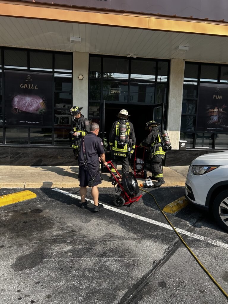 Three firefighters in full gear and SCBAs at the entrance of a commercial storefront.