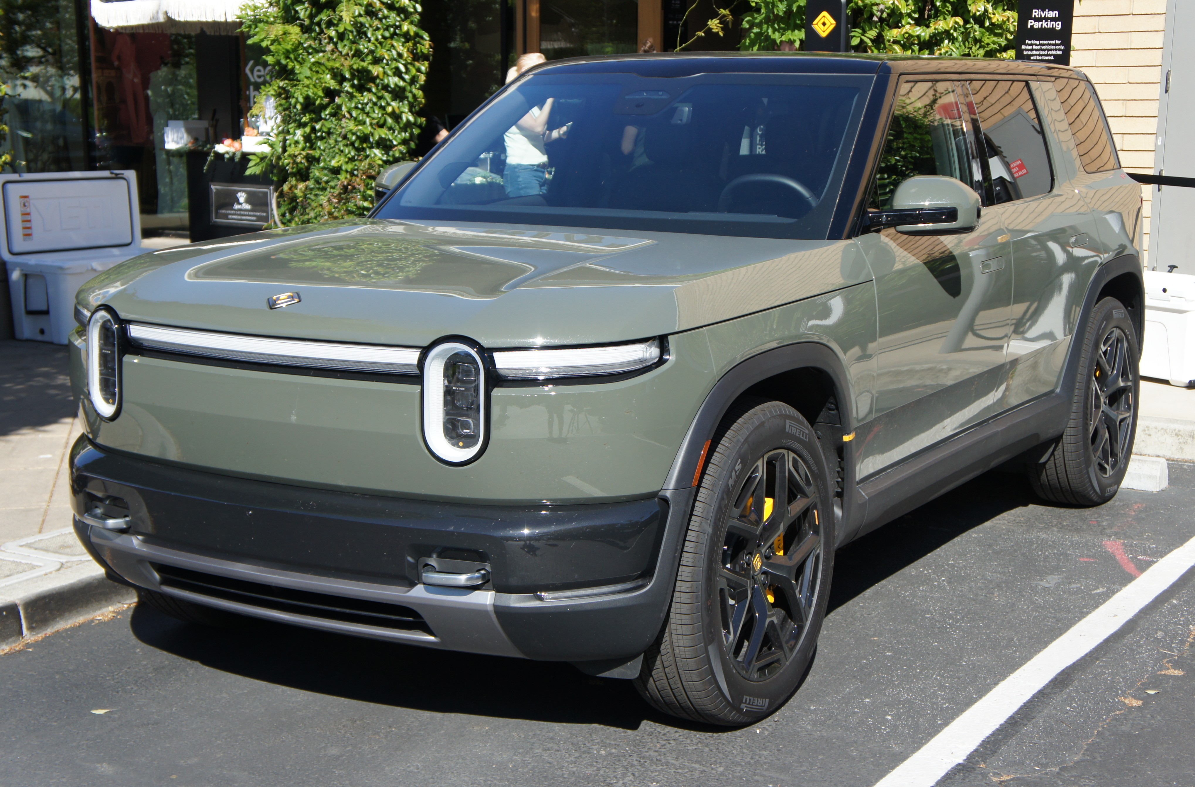 Green Rivian R2 electric SUV parked in a lot, seen from the front-left.