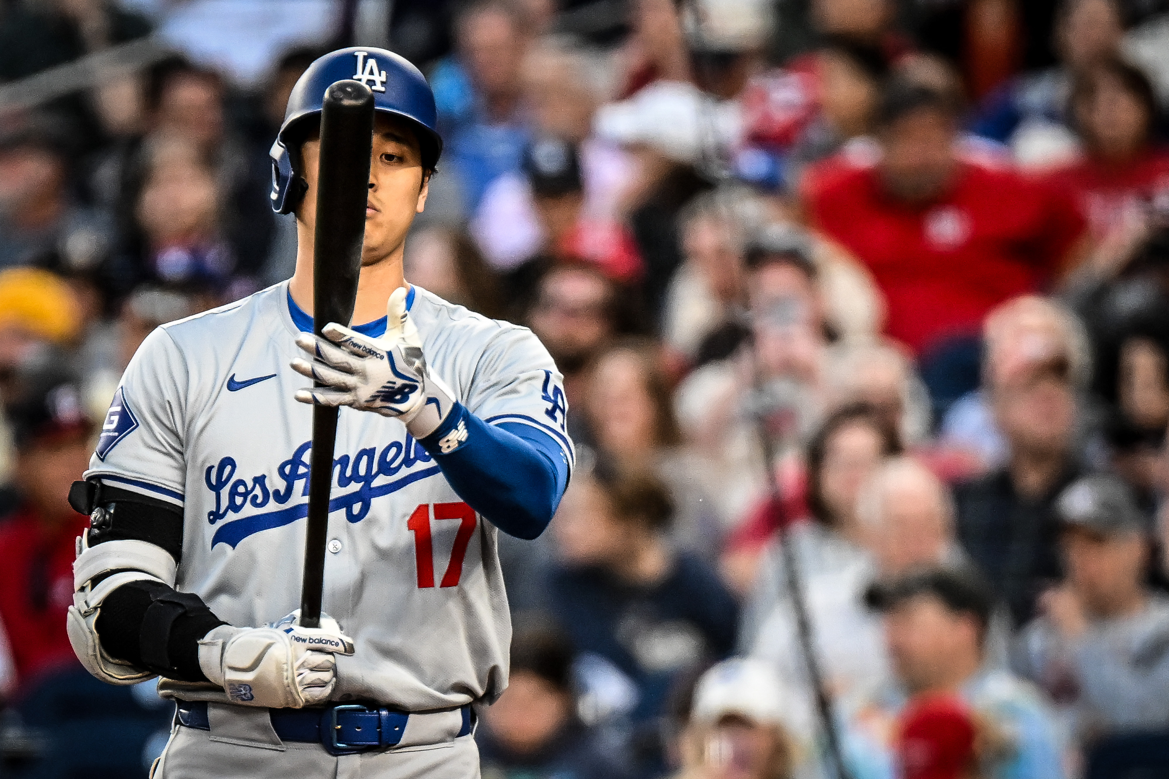 Baseball player in gray Dodgers road uniform number 17 examines his bat at the plate.