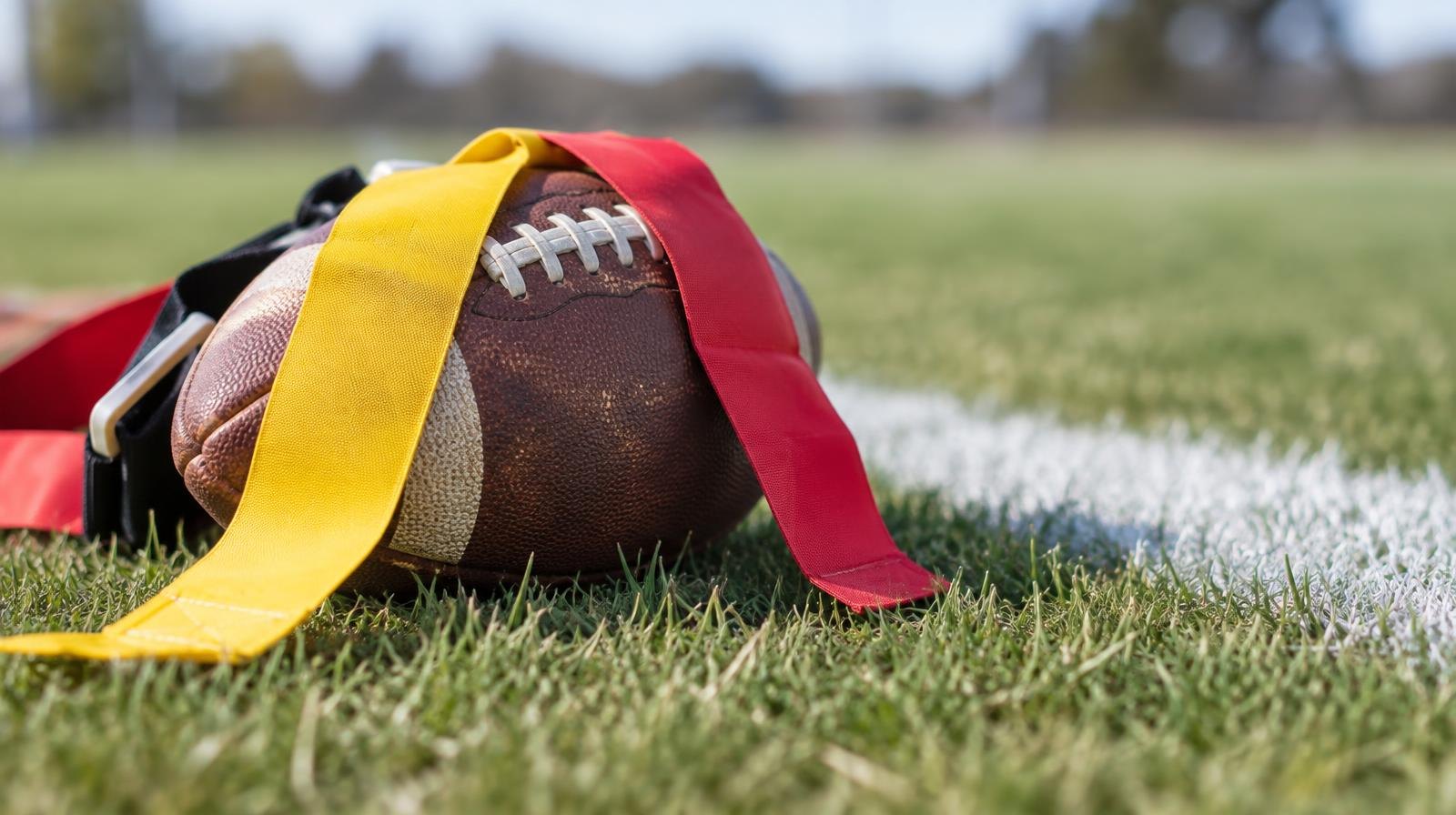 A football with colorful flag belts draped over it on green grass near a white yard line.