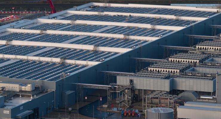 Aerial view of a large data center building with rooftop solar panels and ground-level cooling equipment.