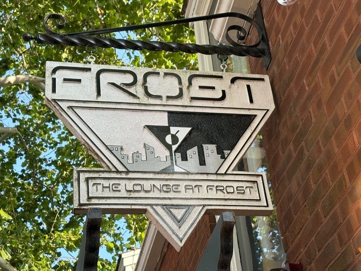 Decorative metal sign reading 'Frost' and 'The Lounge at Frost' on a brick building exterior.