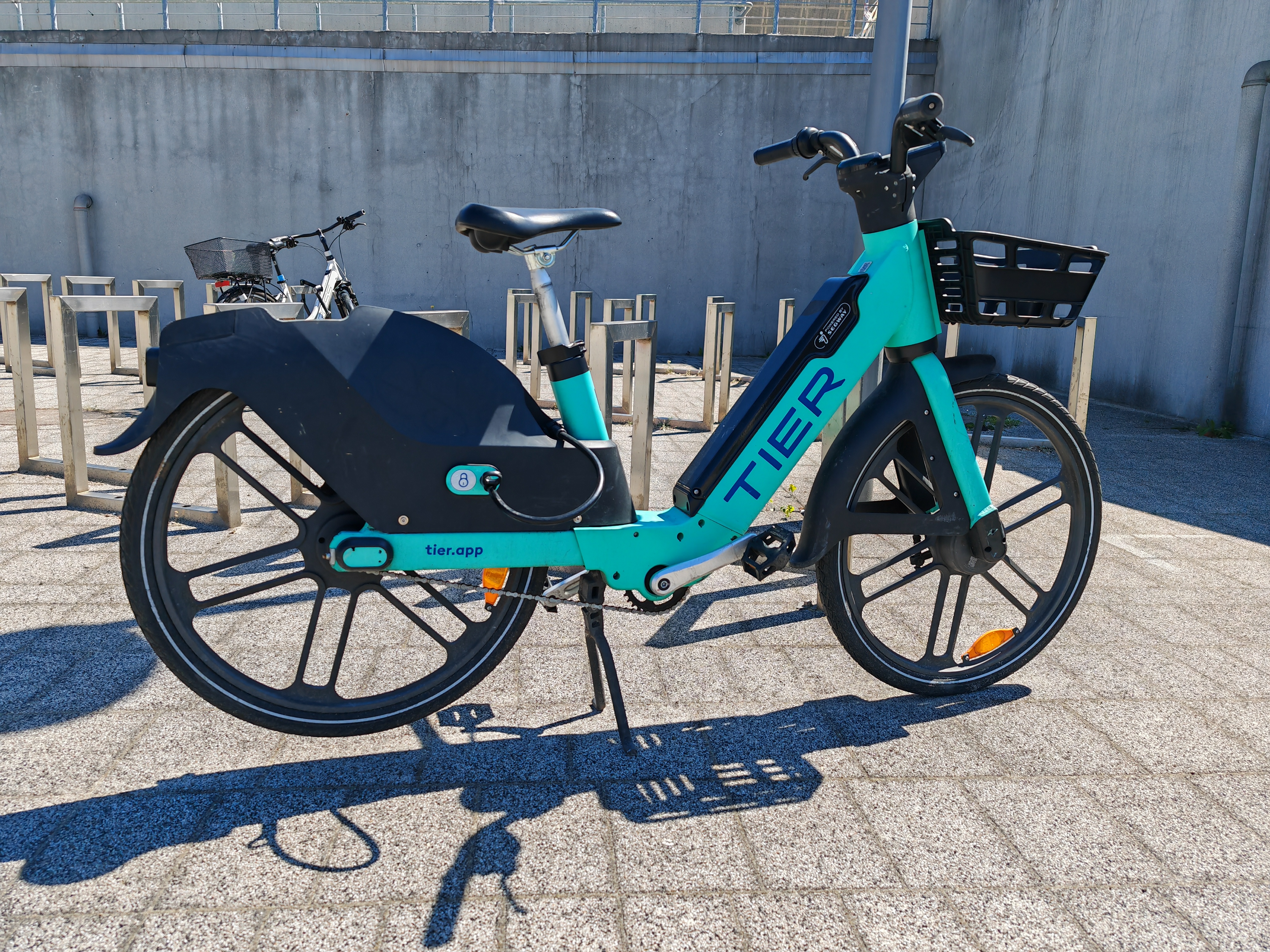 A teal electric bicycle with a front basket parked near bike racks outdoors.