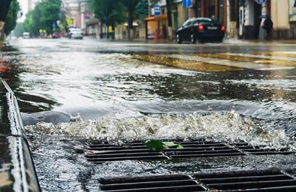 Water flowing rapidly into a metal storm drain grate on a wet urban street.