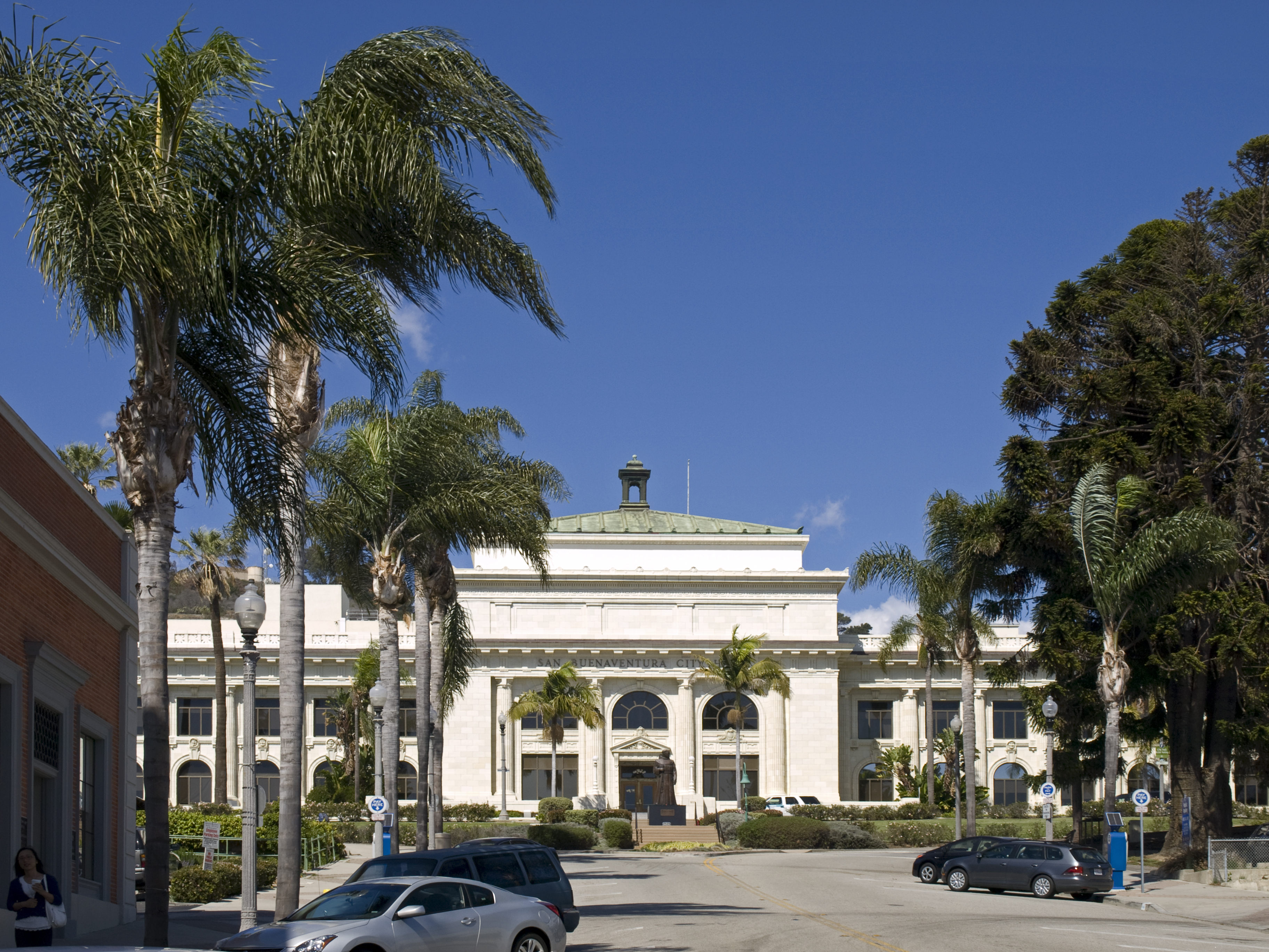 Large white neoclassical courthouse with a green dome flanked by tall palm trees.