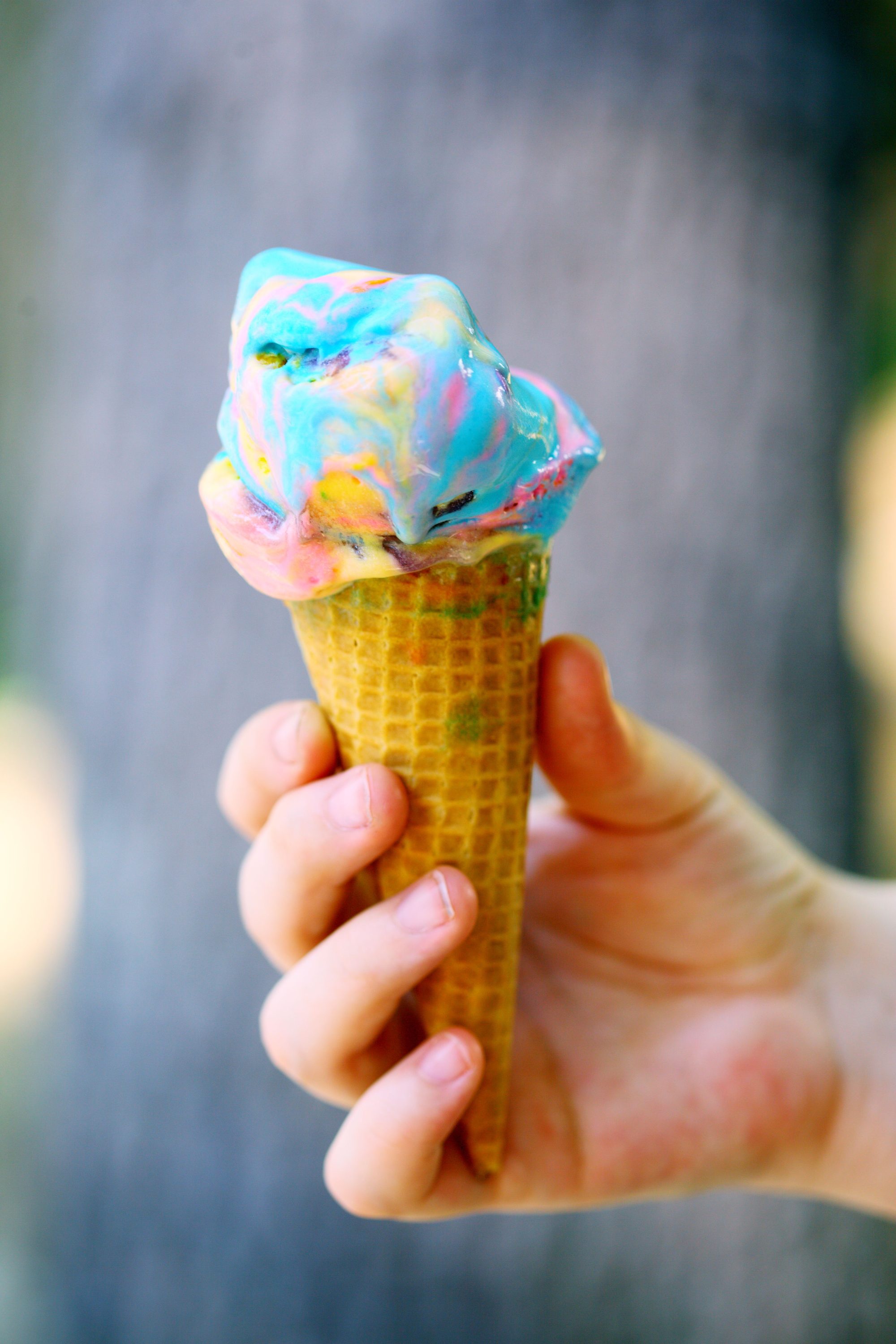 Close-up of a multicolored ice cream cone held in a child's hand with a blurred background.