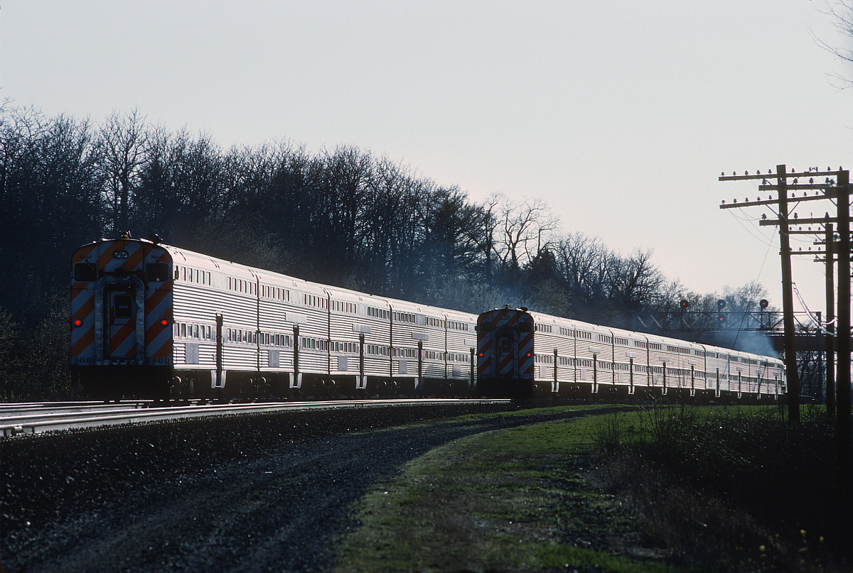 Metra commuter train with silver bi-level cars traveling along a rail line.