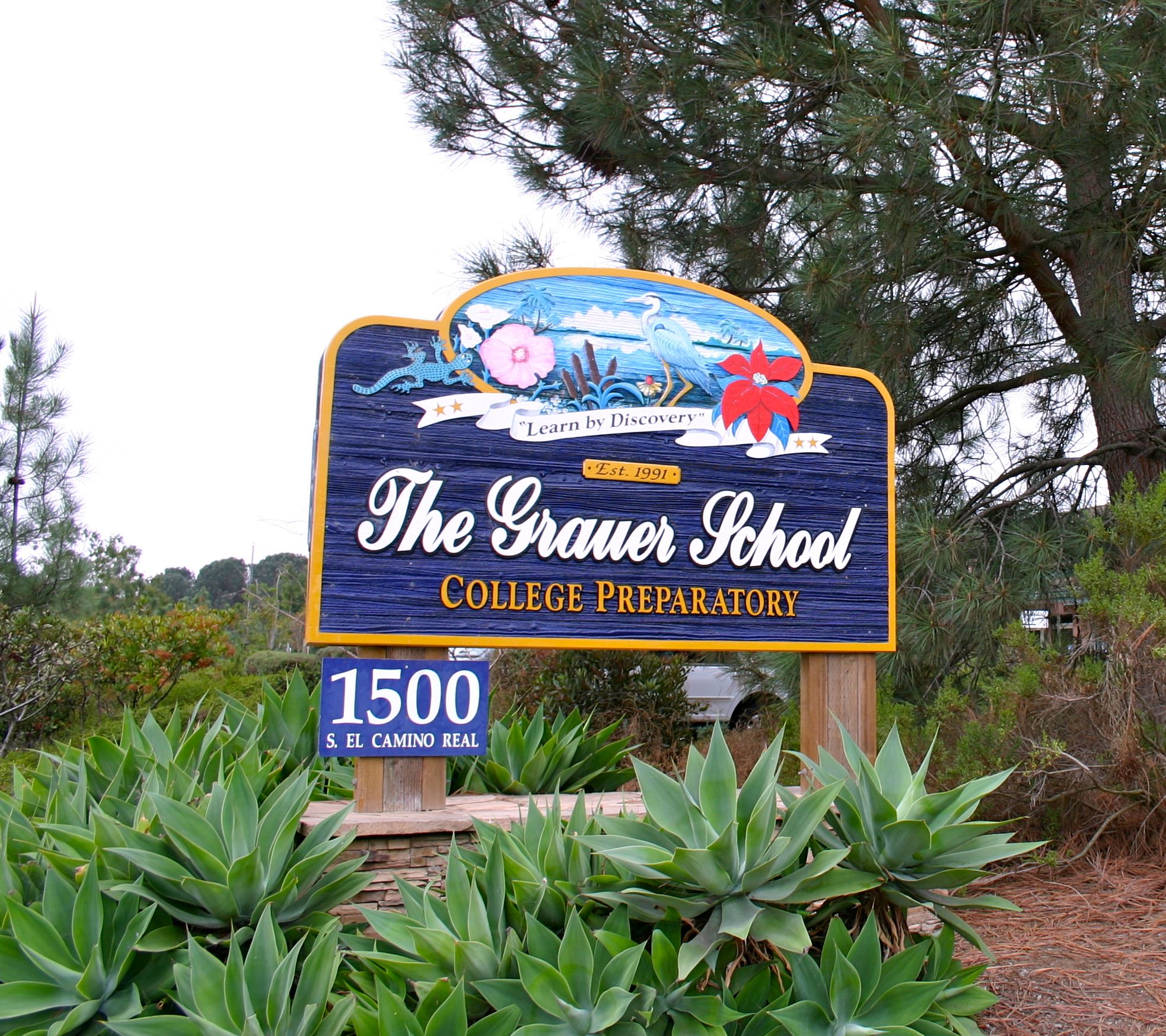 Wooden school entrance sign reading 'The Grauer School College Preparatory' surrounded by agave plants.