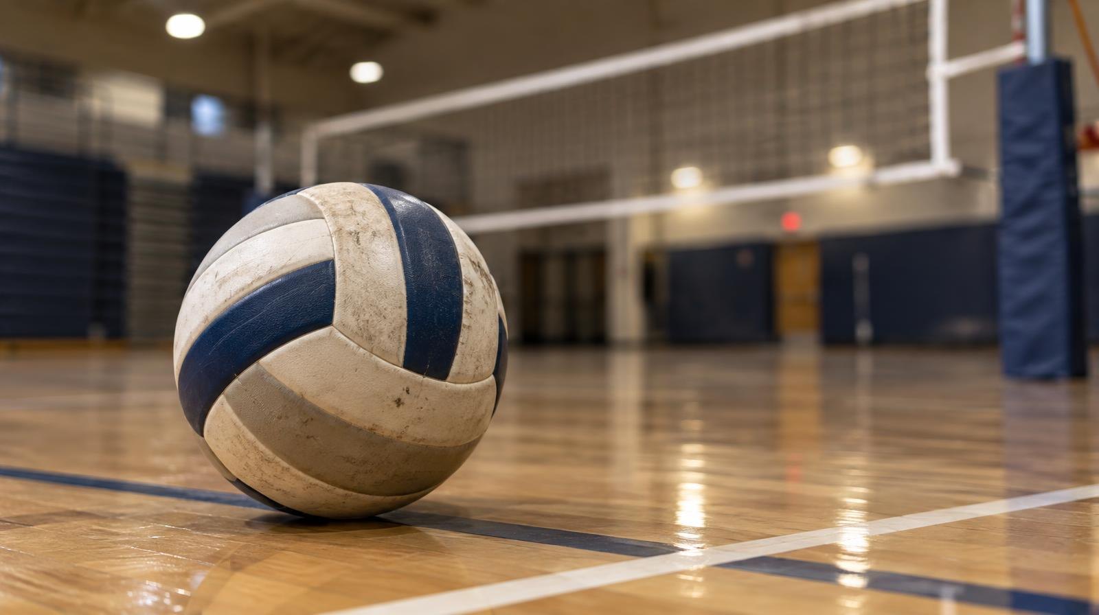 A volleyball resting on a hardwood gym floor near the net.
