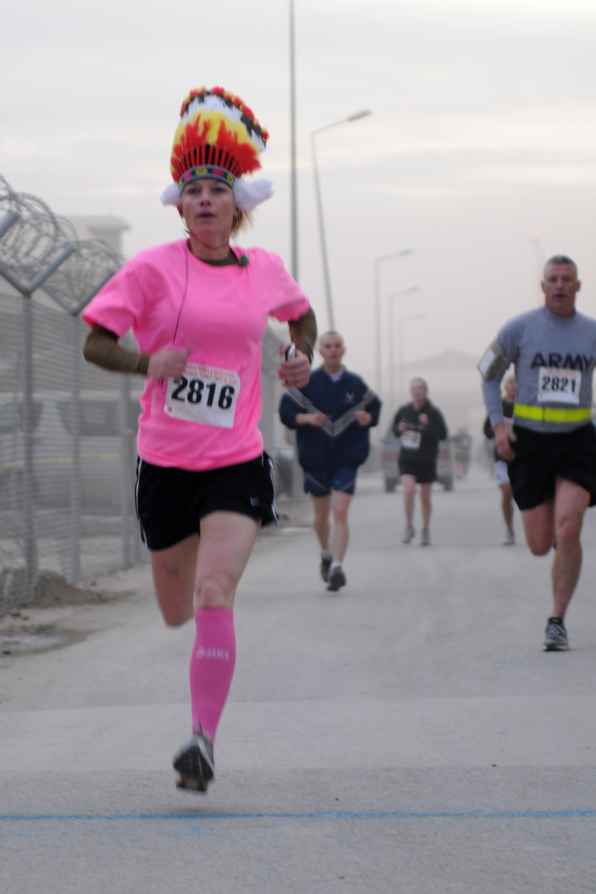 A costumed runner in a pink shirt leads a pack of runners in a 5K race.