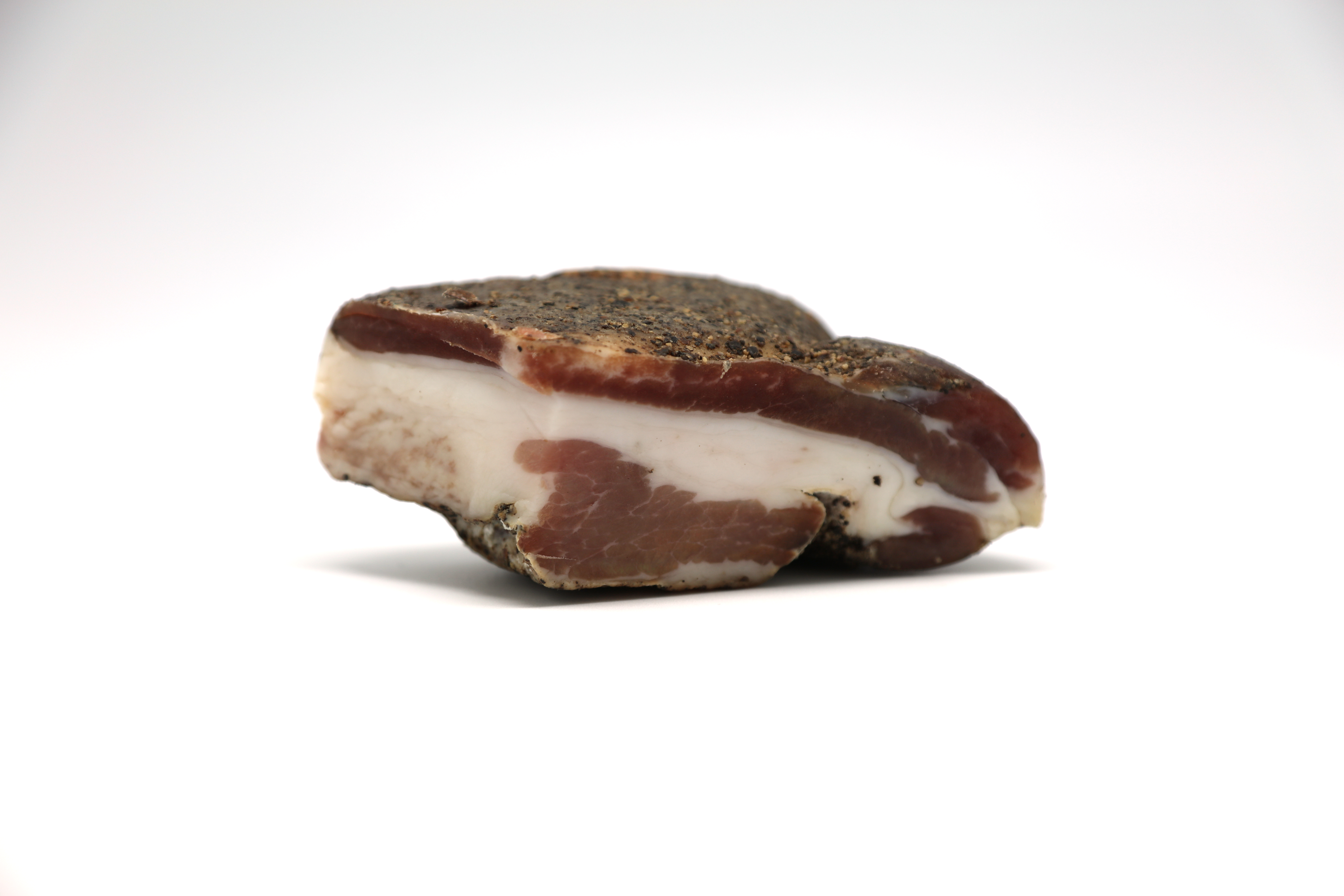 Cross-section of cured pork jowl showing layers of meat and fat with a dark spiced rind.