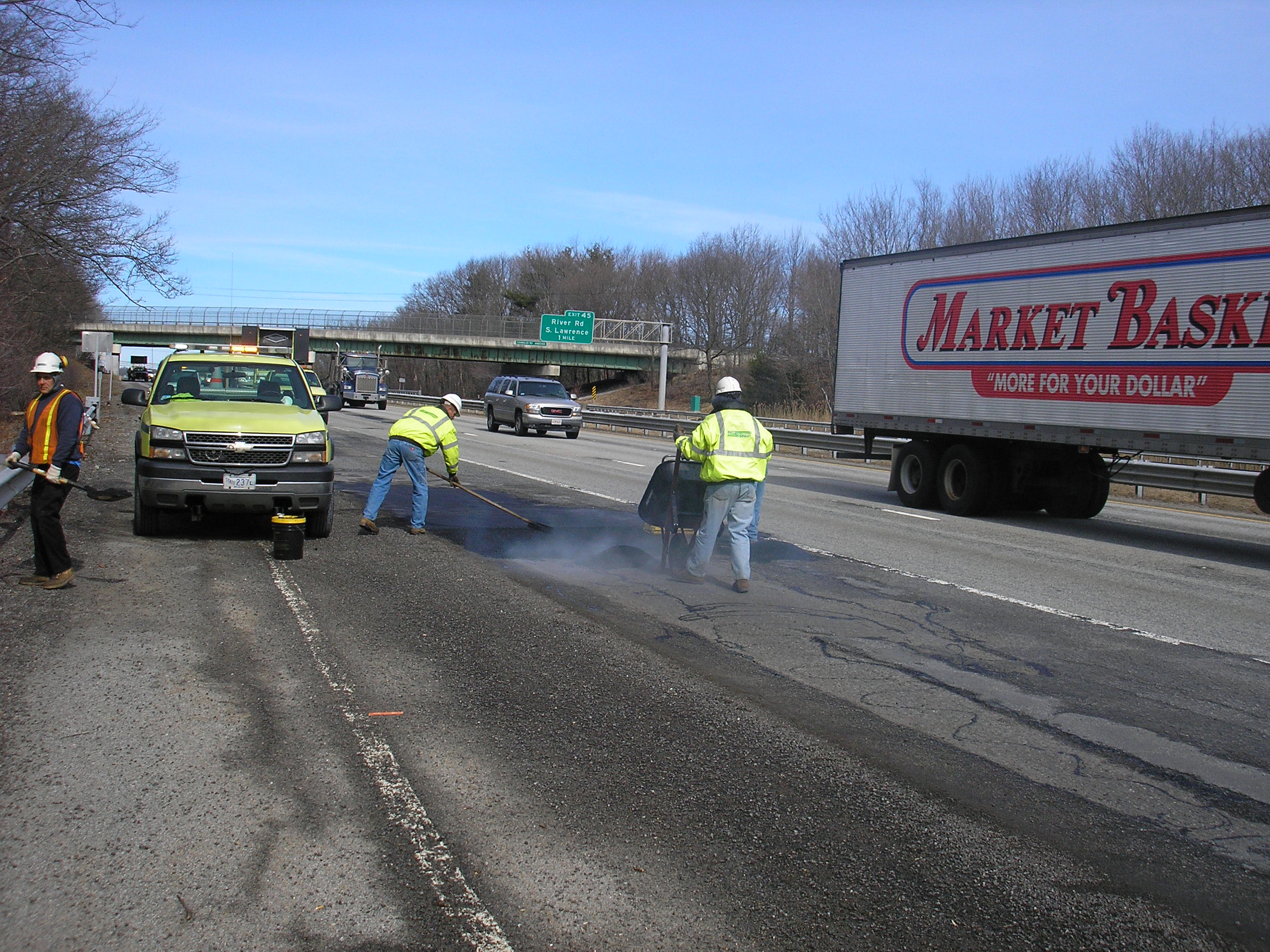 Workers in safety vests fill a pothole on a busy highway.