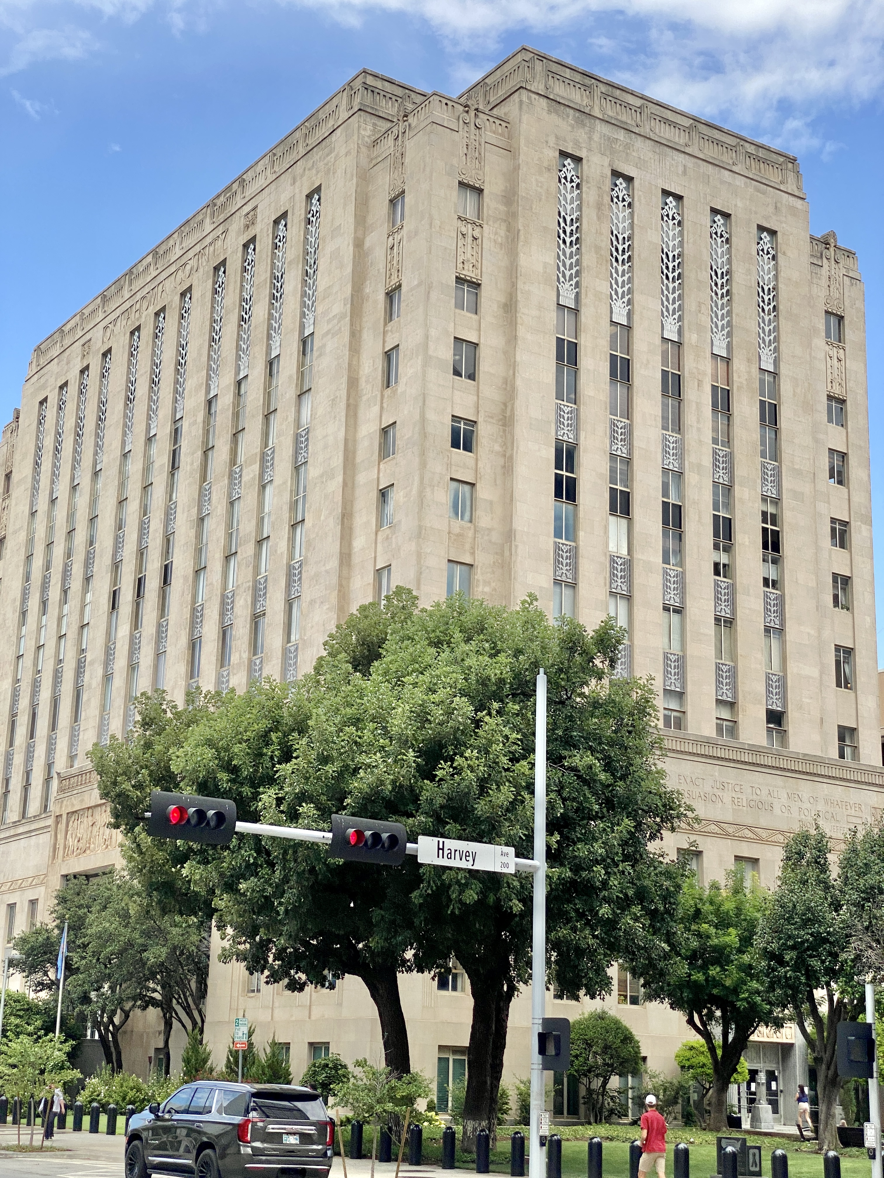 Multi-story Art Deco government building at a street corner under partly cloudy sky.