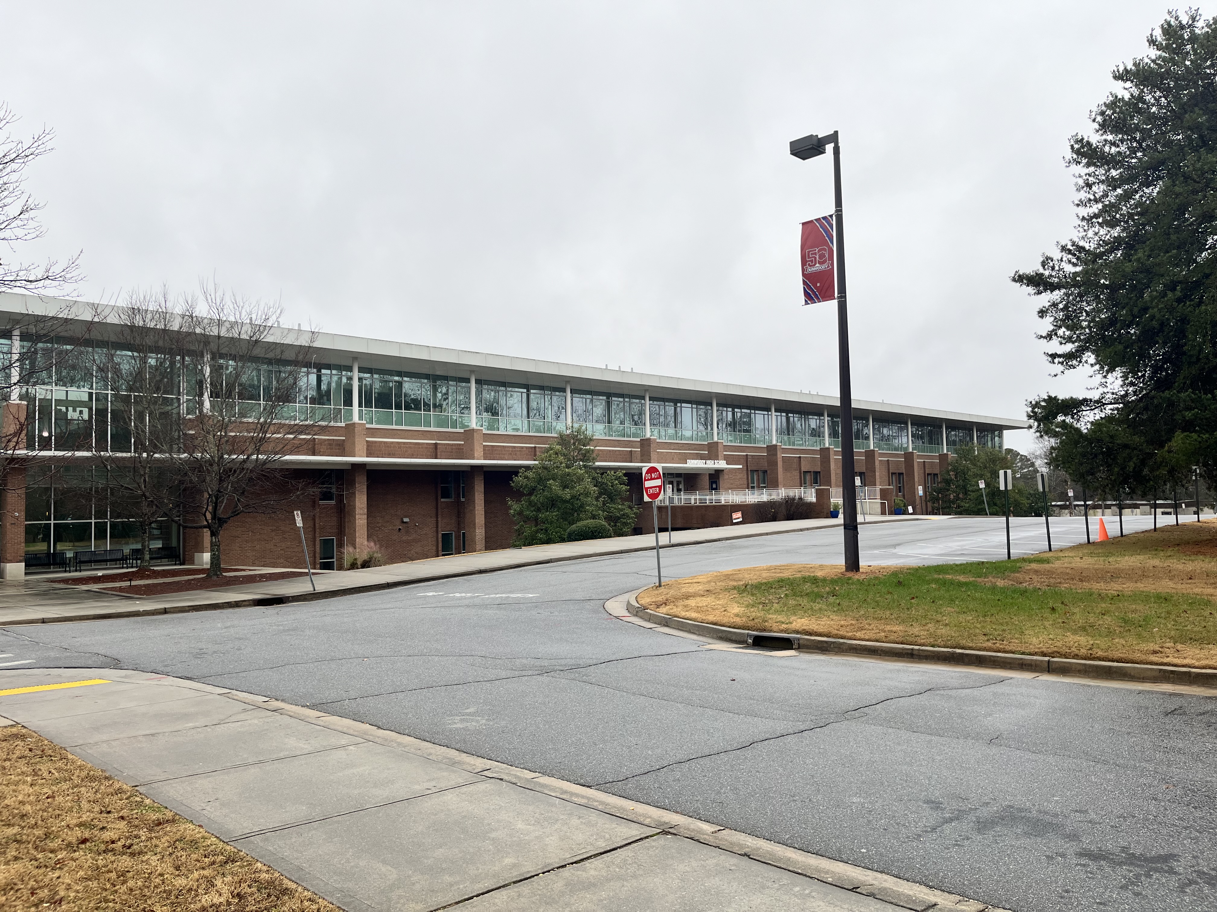 Two-story brick and glass school building with a wide parking lot under overcast skies.