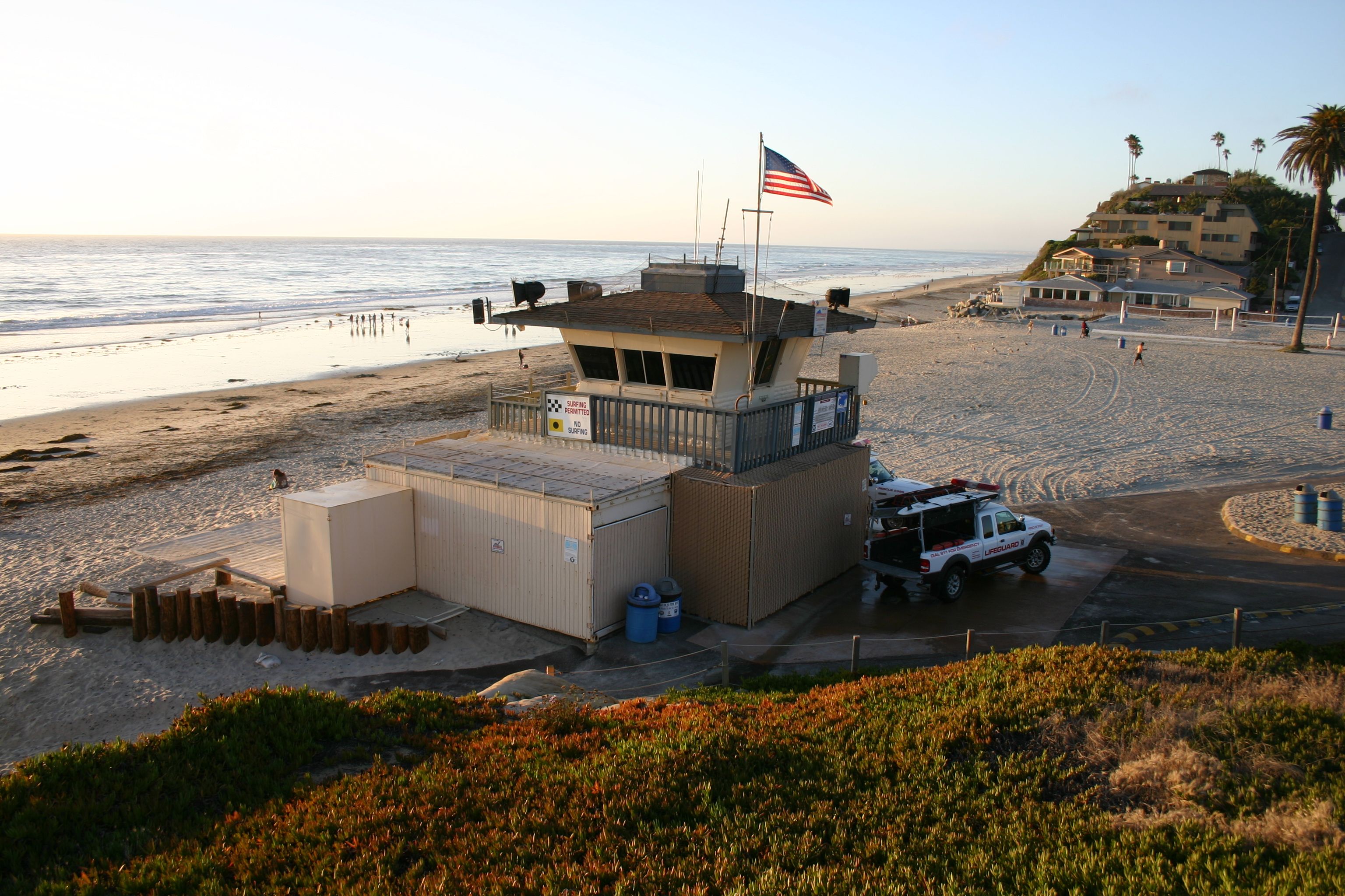 Lifeguard station building on a sandy beach with a white vehicle parked beside it.