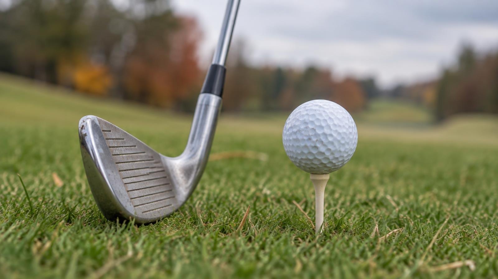 A golf ball on a tee in short grass beside an iron club head.