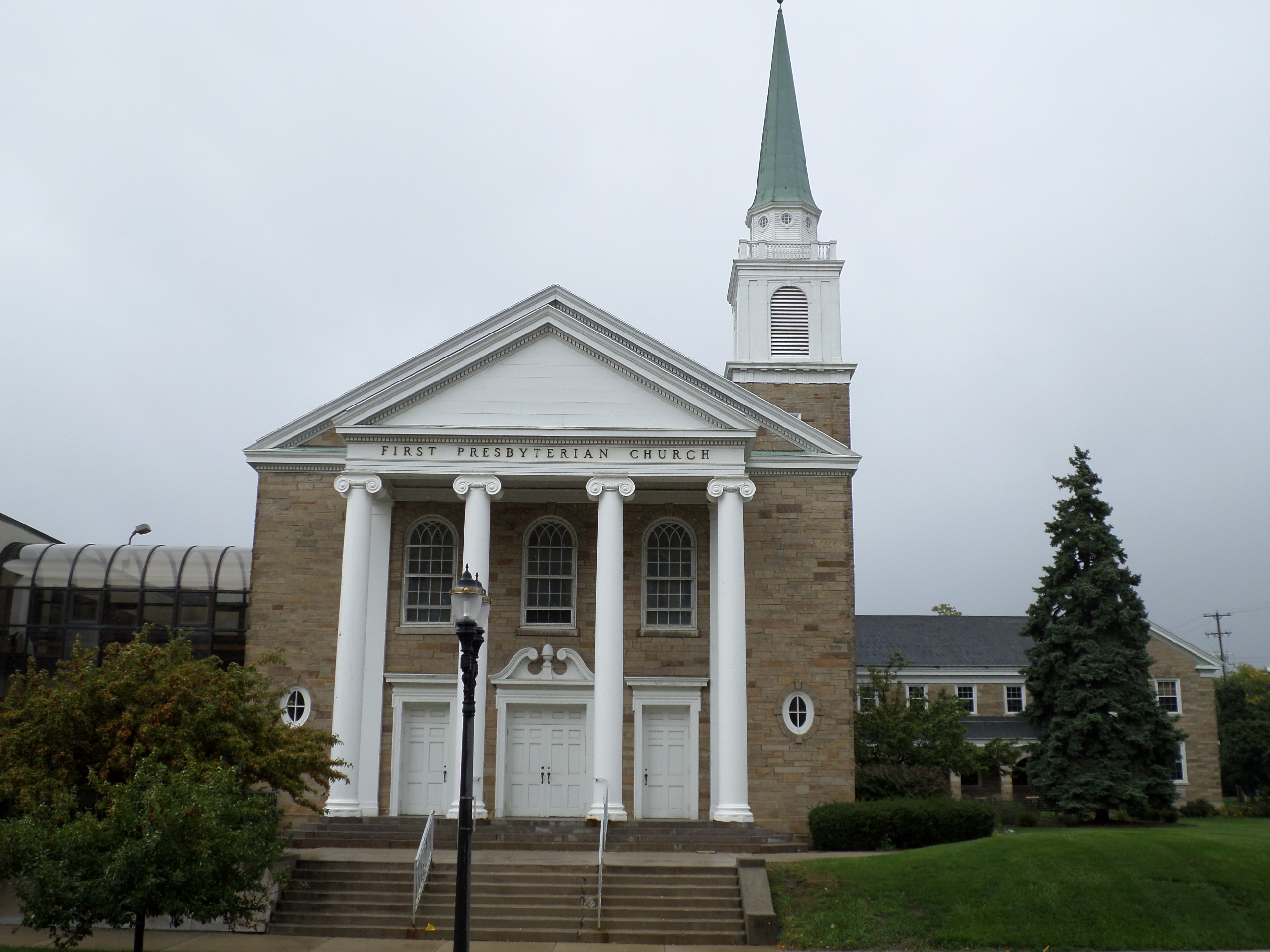 Stone church with white classical columns and a green-capped steeple, steps at the entrance.
