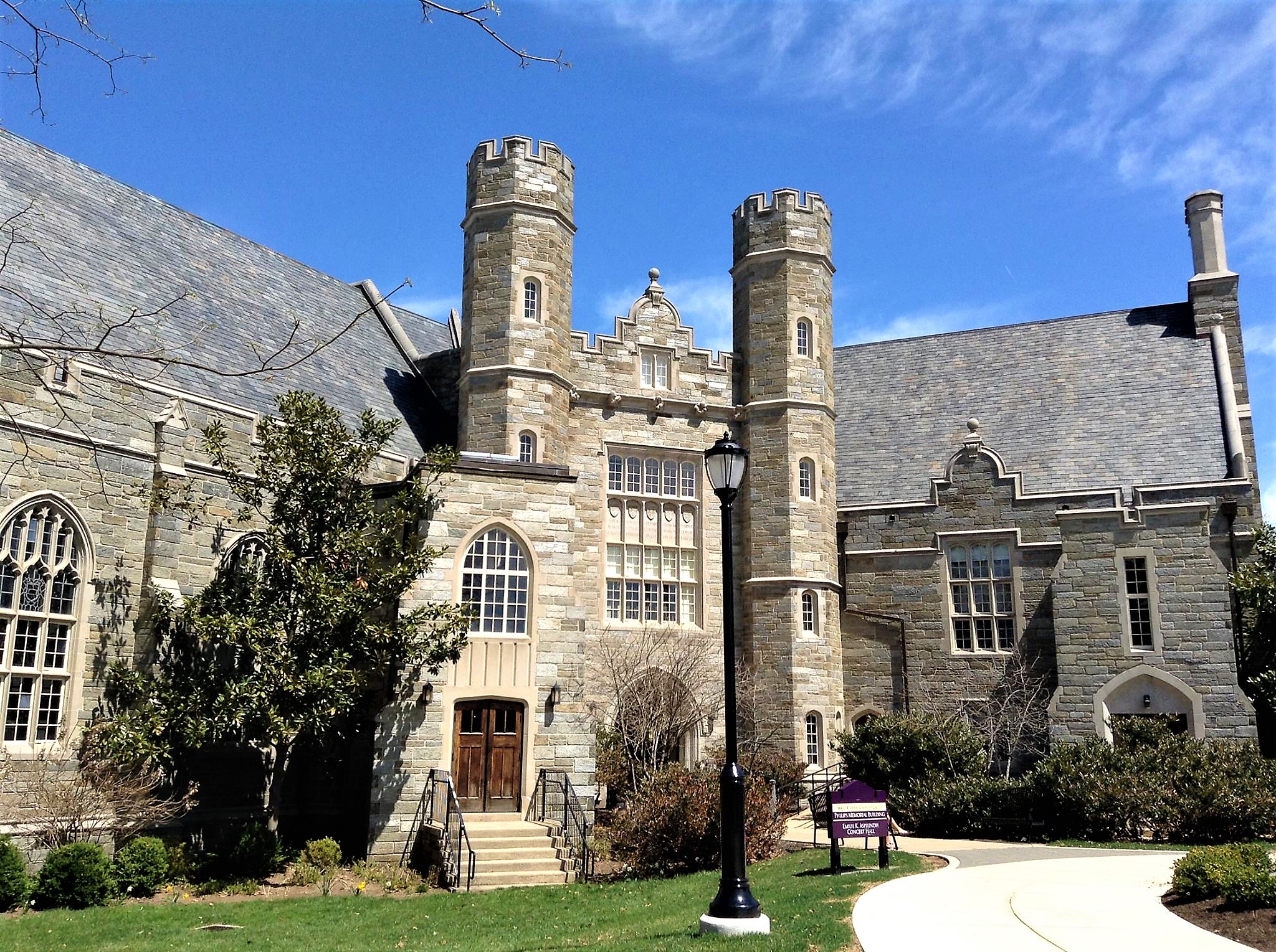 Gothic stone university building with twin towers under a blue sky.