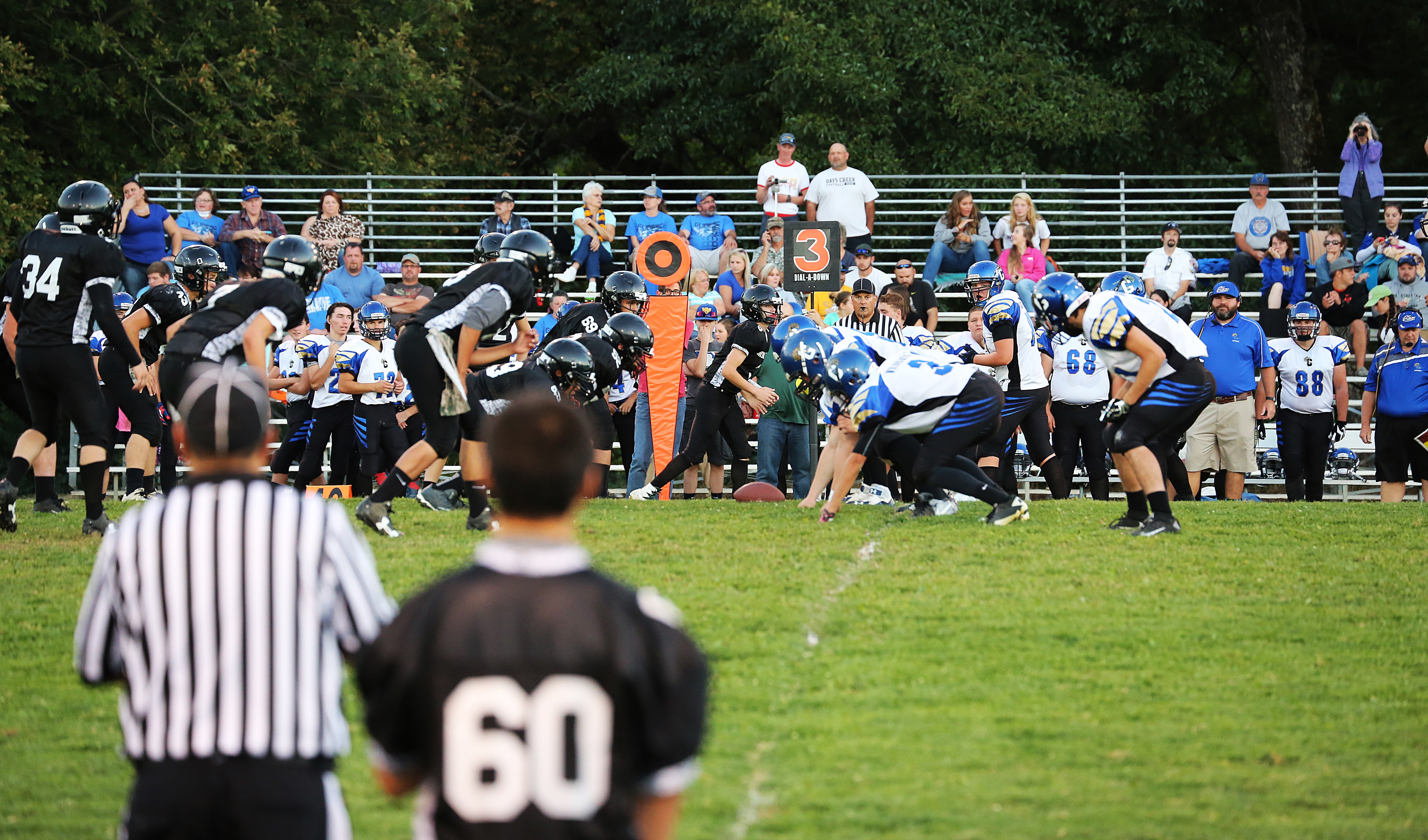 Football players in dark uniforms lined up at the line of scrimmage on a grass field.