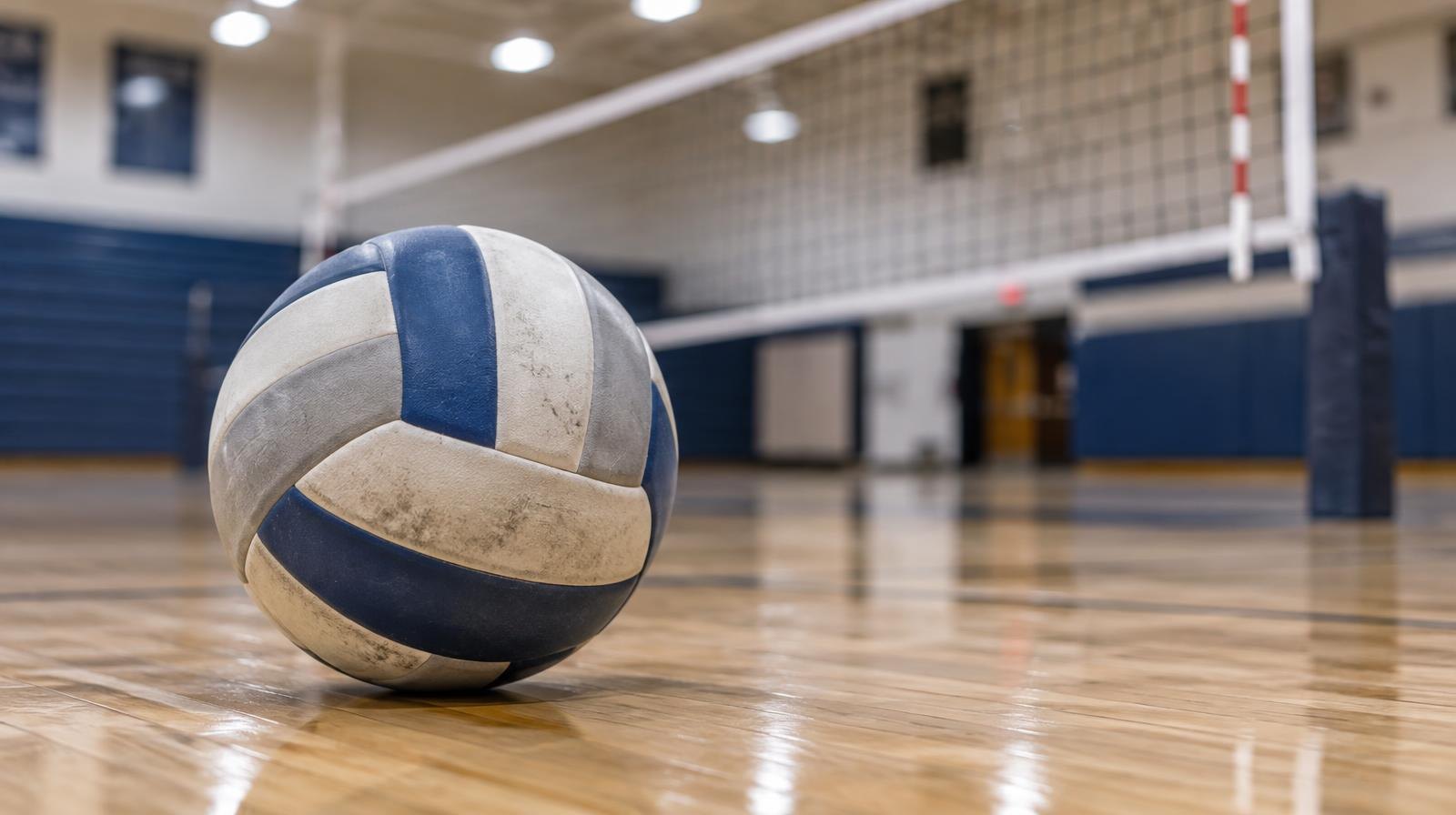 A volleyball resting on a hardwood gym floor near a net.