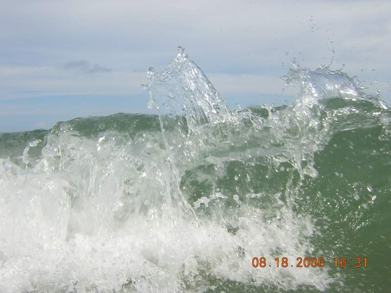 A breaking ocean wave crashes with white foam and spray against an overcast sky.