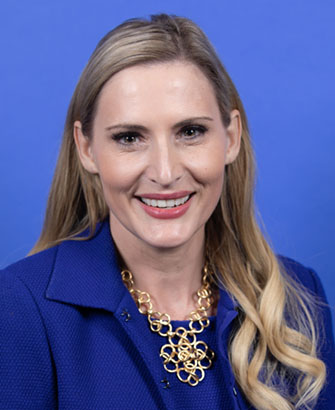 Woman in a blue blazer poses for an official congressional portrait against a blue background.
