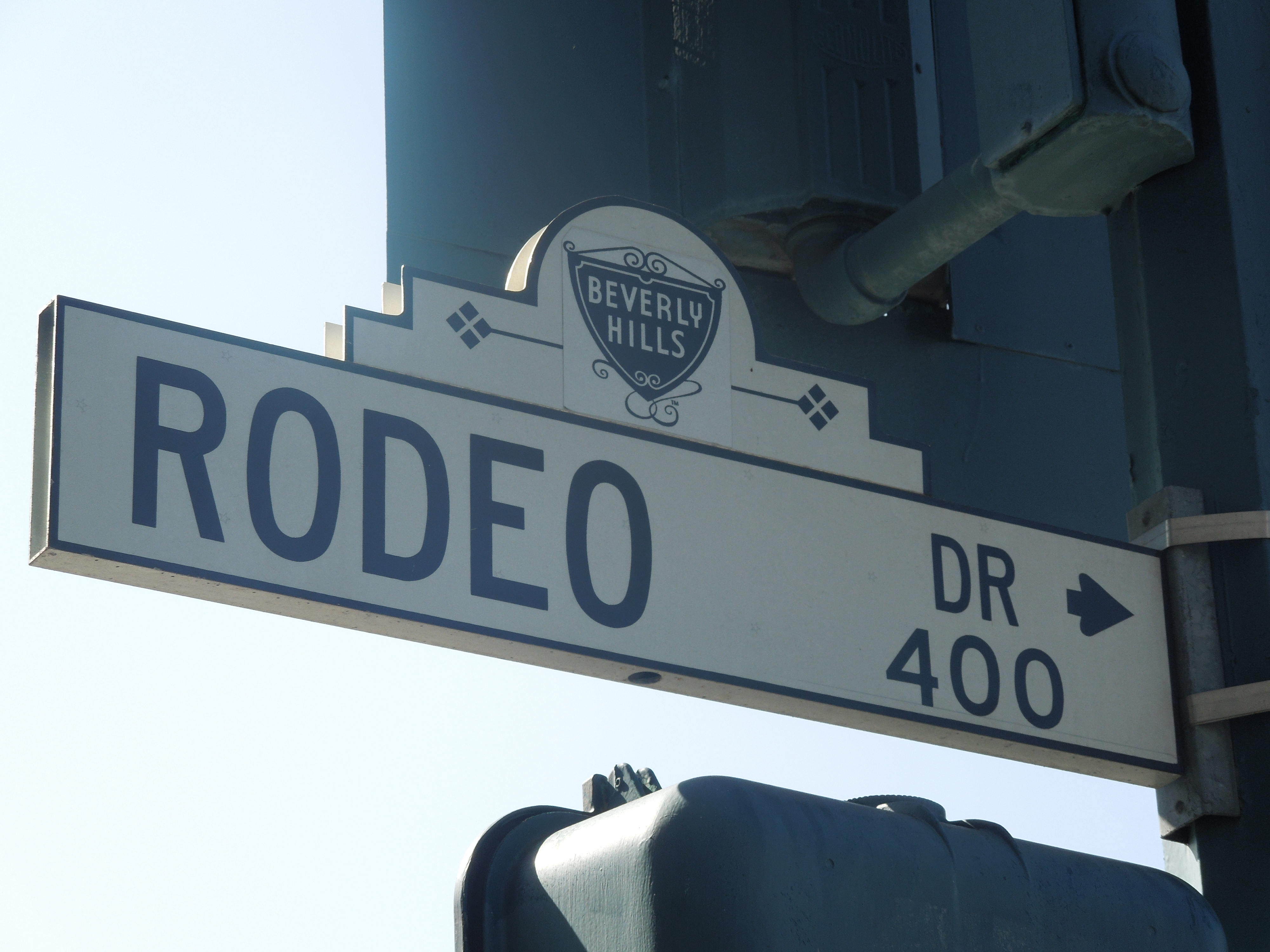 White street sign reading Rodeo Drive with a Beverly Hills city emblem mounted on a pole.