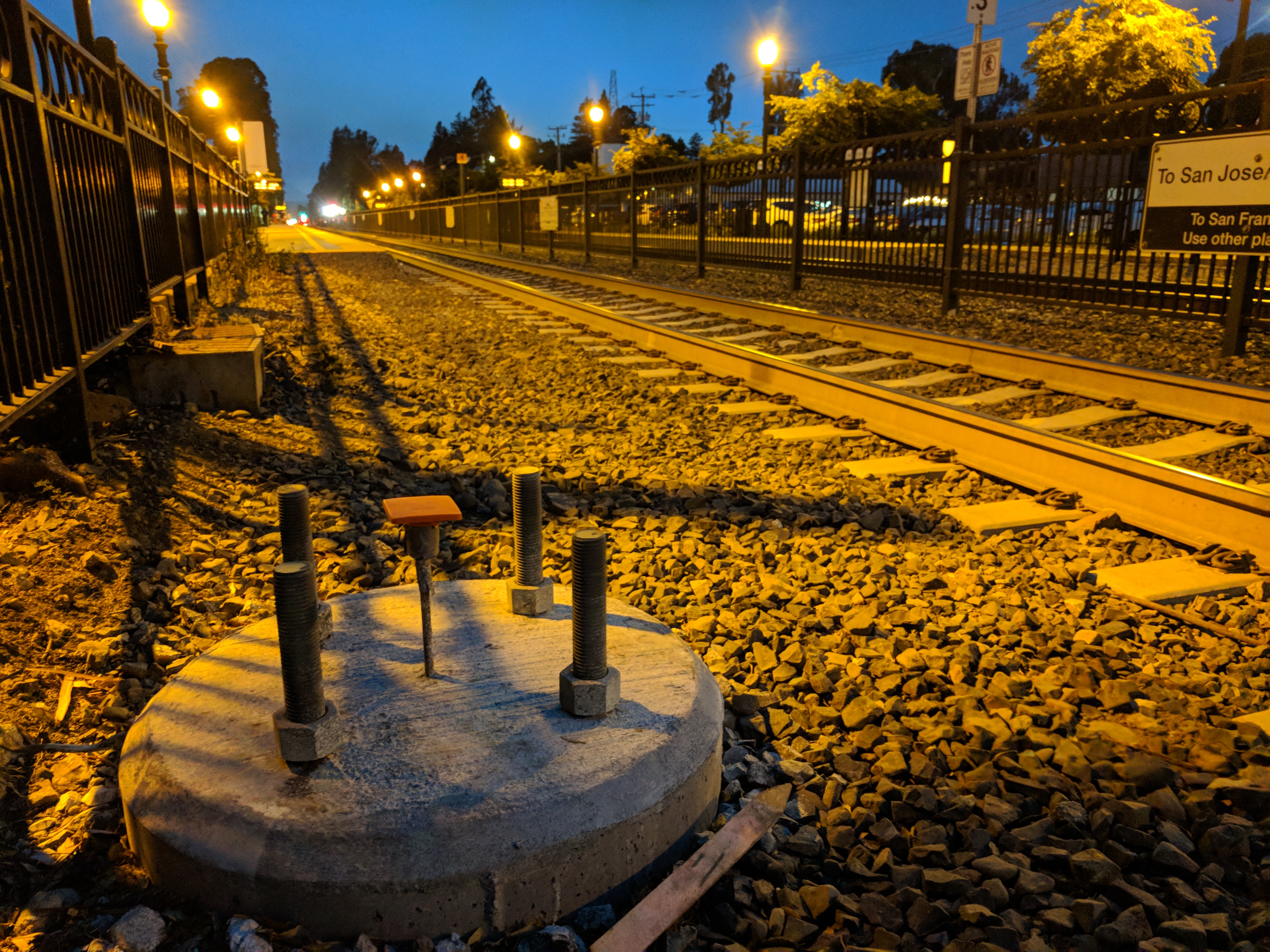 Caltrain tracks at night with a station sign reading 'To San José' and amber street lights