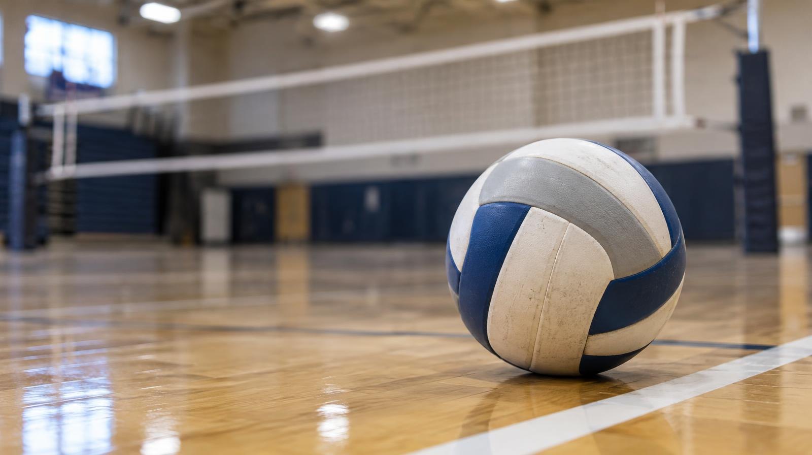 A volleyball resting on a hardwood gym floor beside a white boundary line.