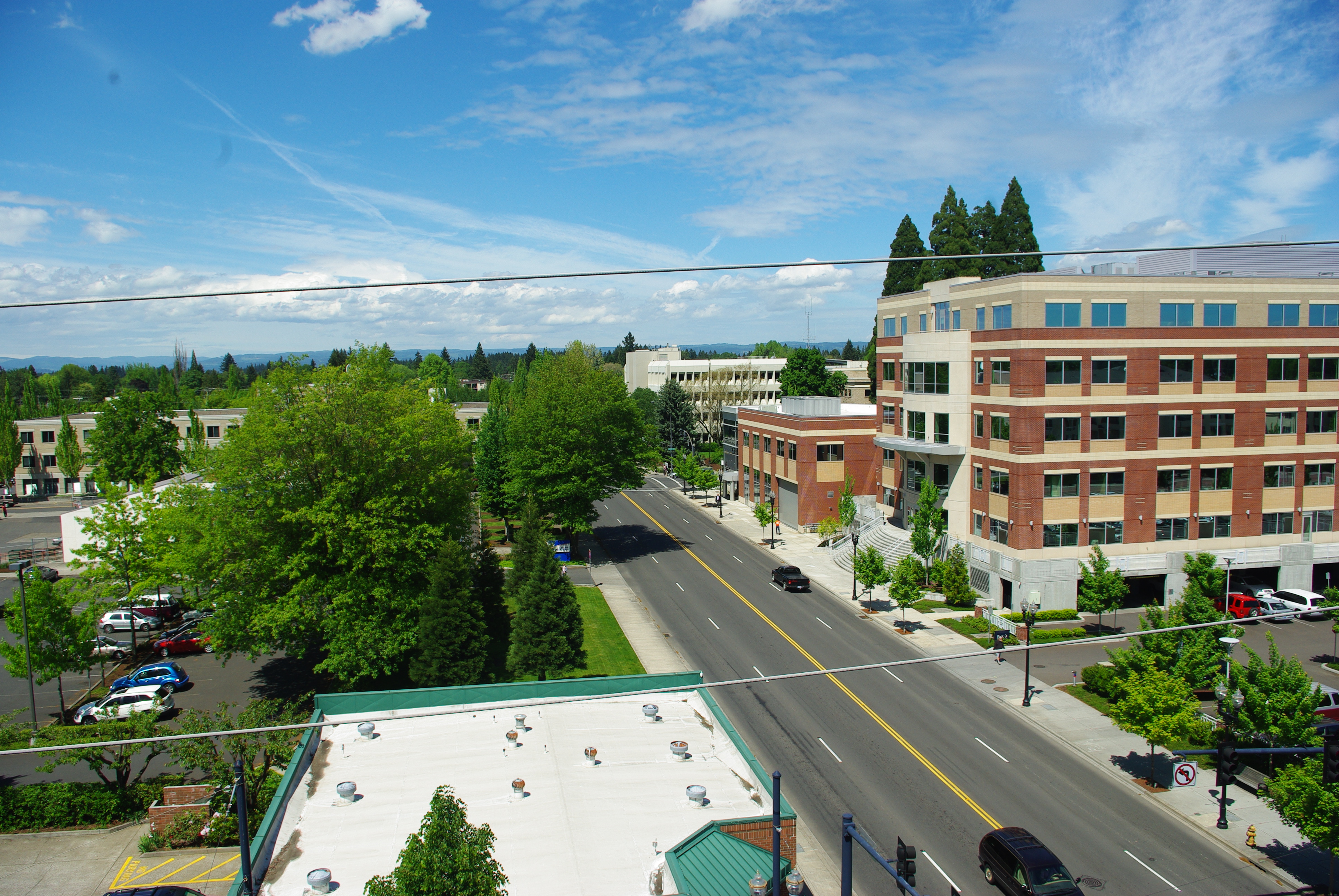 Elevated view of a downtown street lined with brick buildings, trees, and parked cars.